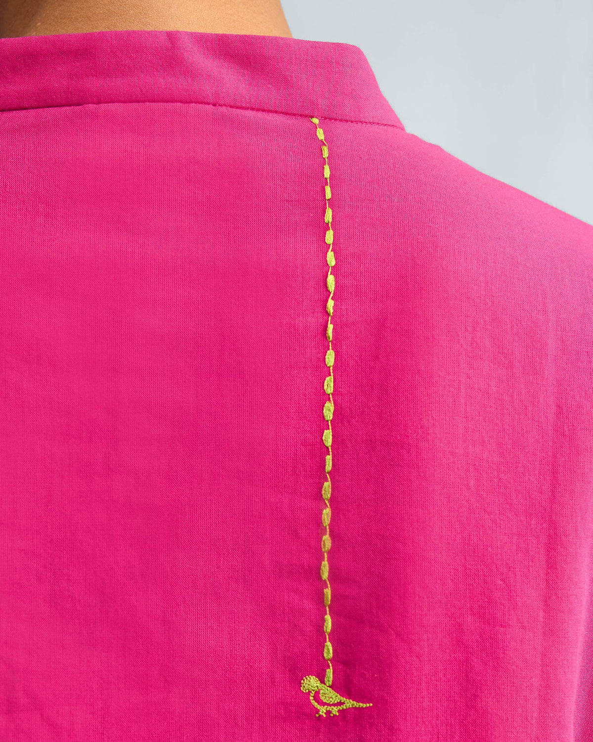 Close-up of lime green bird embroidery on the back of a fuchsia kurta.