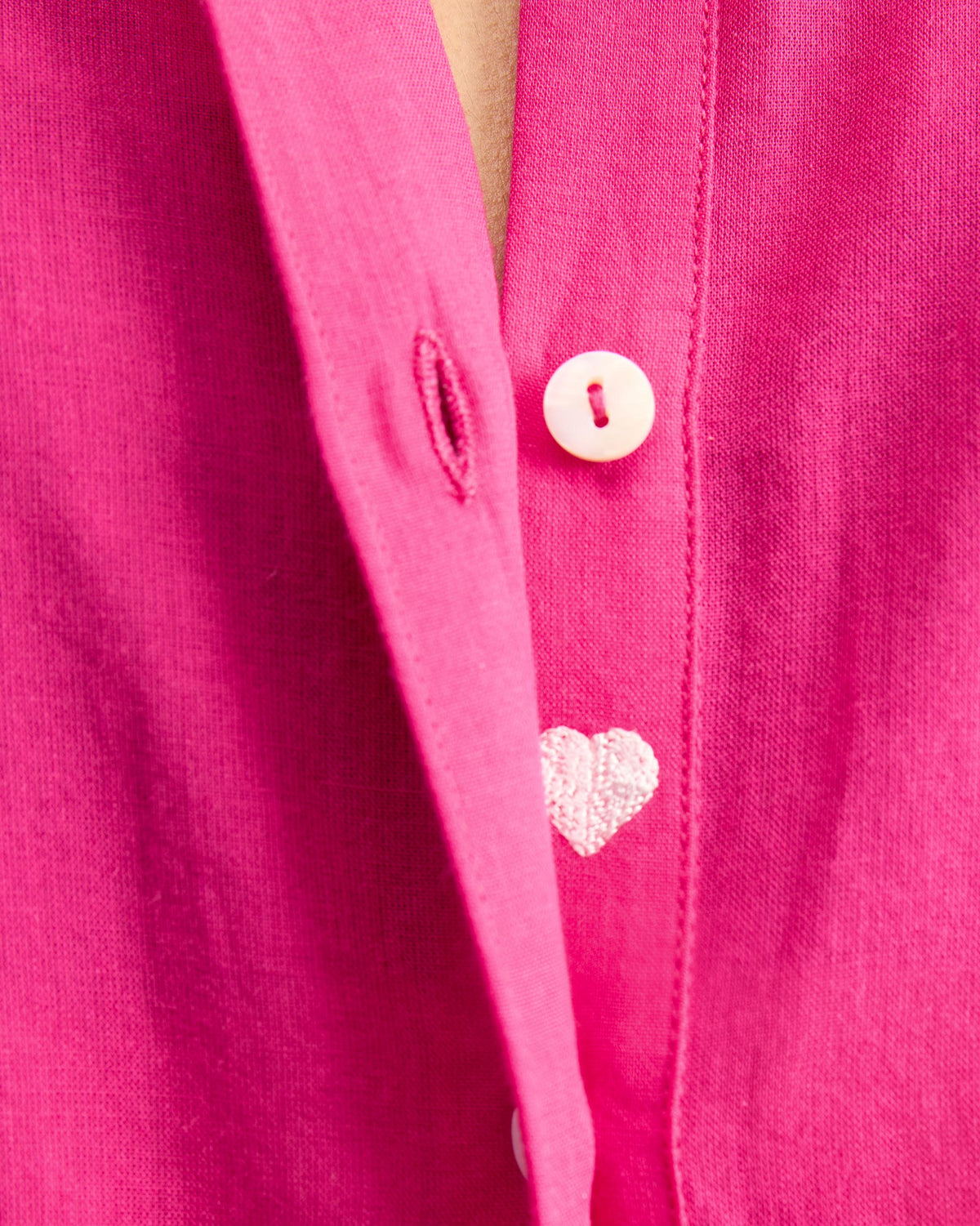 Close-up of a white heart embroidery beside a button on a fuchsia kurta.