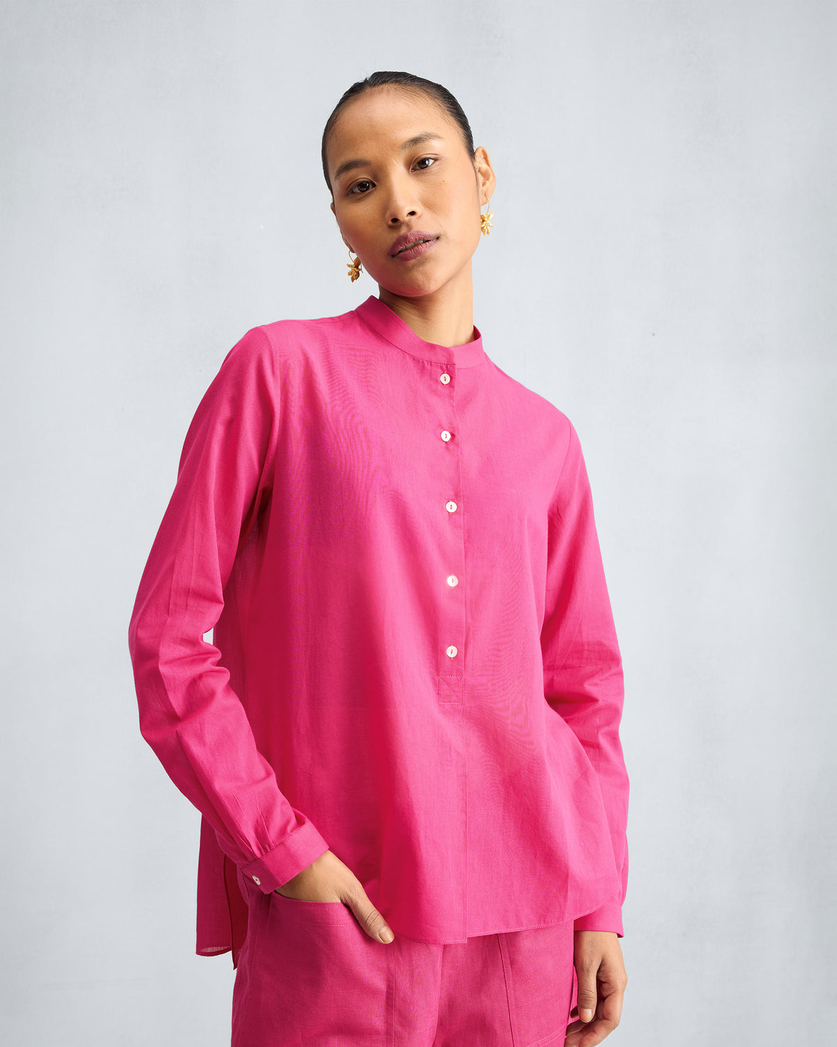 Person wearing a fuchsia mandarin collar top with a hand in the pocket.