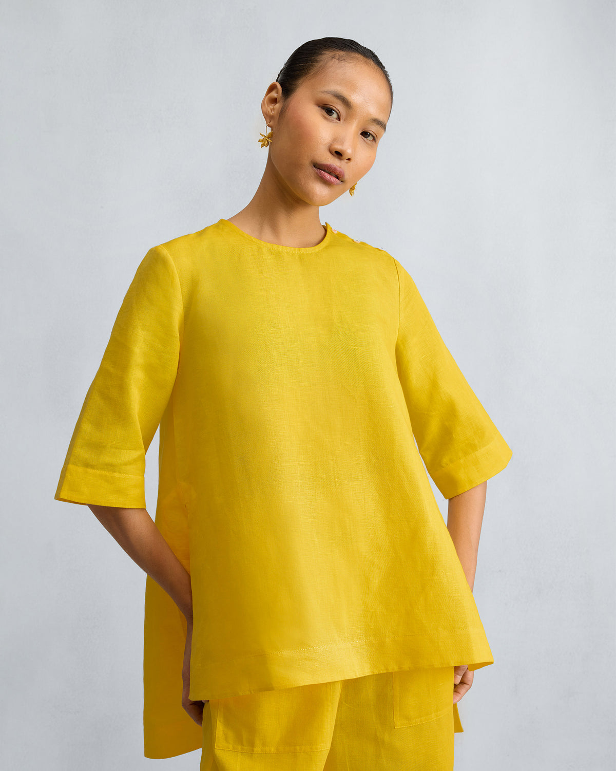 Yellow high slit top with shoulder buttons and a flared high-low hem.