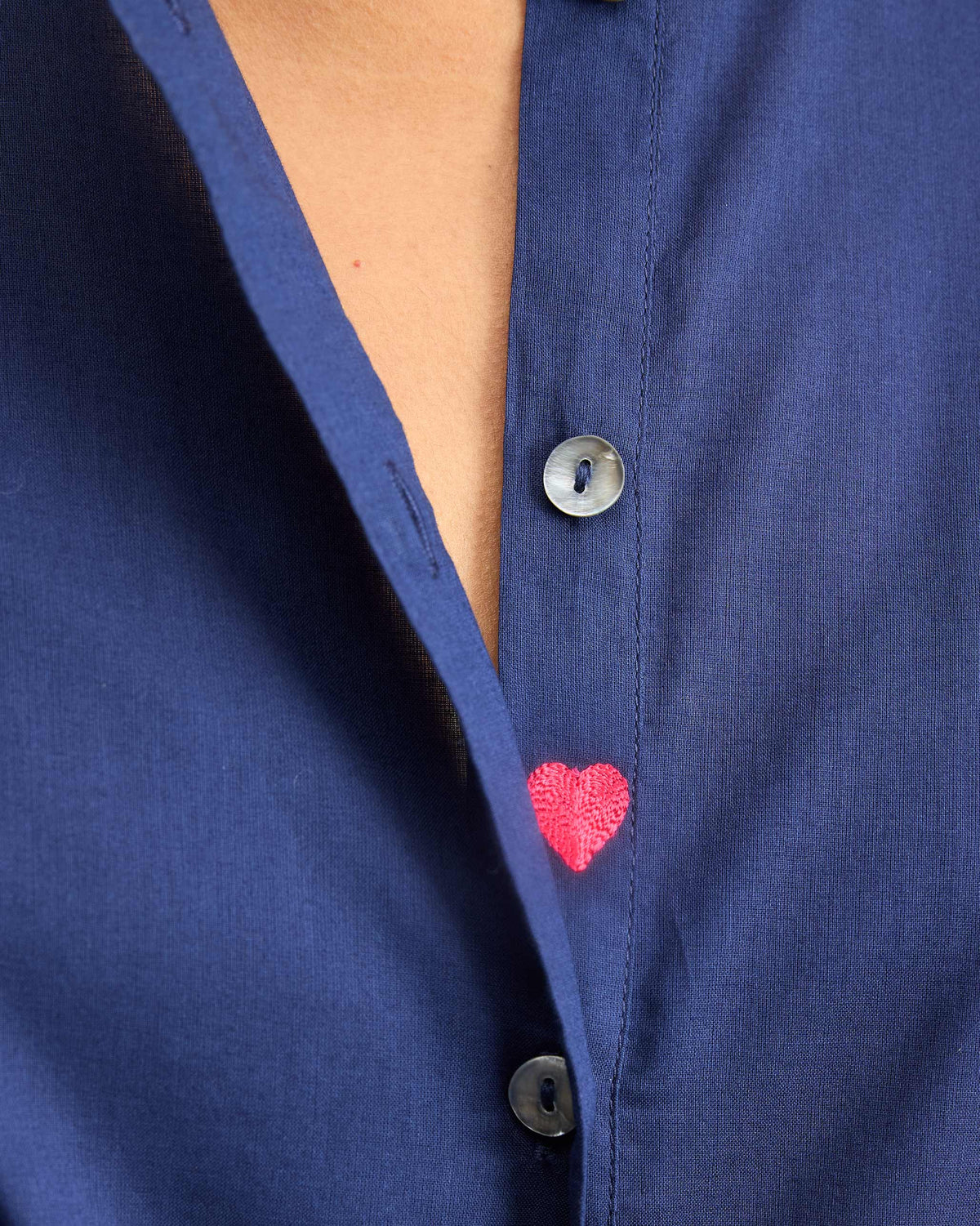 Close-up of a pink heart embroidery beside buttons on an ink blue top.