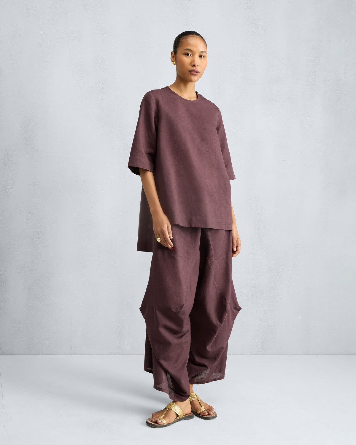 Person wearing a chocolate plum high slit top set with draped pants.