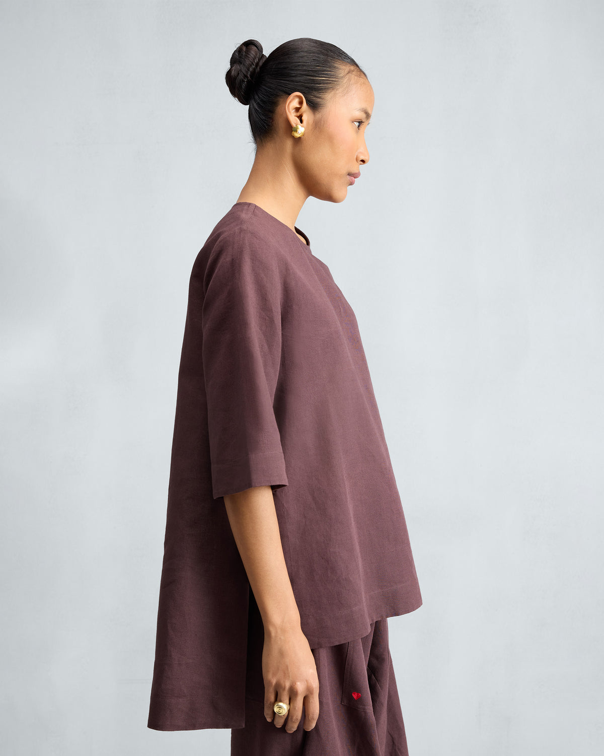 Side view of a chocolate plum high slit top showing the high-low hem.