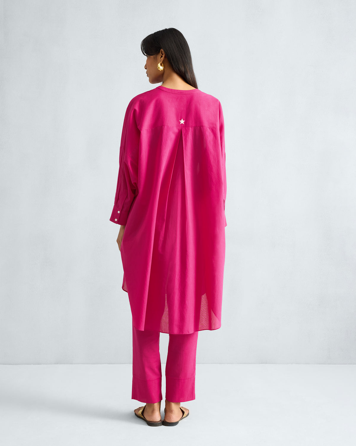 Back of a fuchsia Lazy Sunday tunic with a white embroidered star and box pleat.