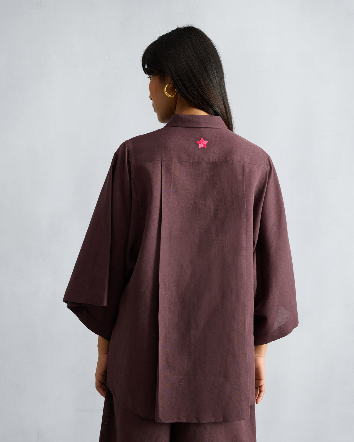 Back of a chocolate plum drop-armhole shirt with a box pleat and pink star.
