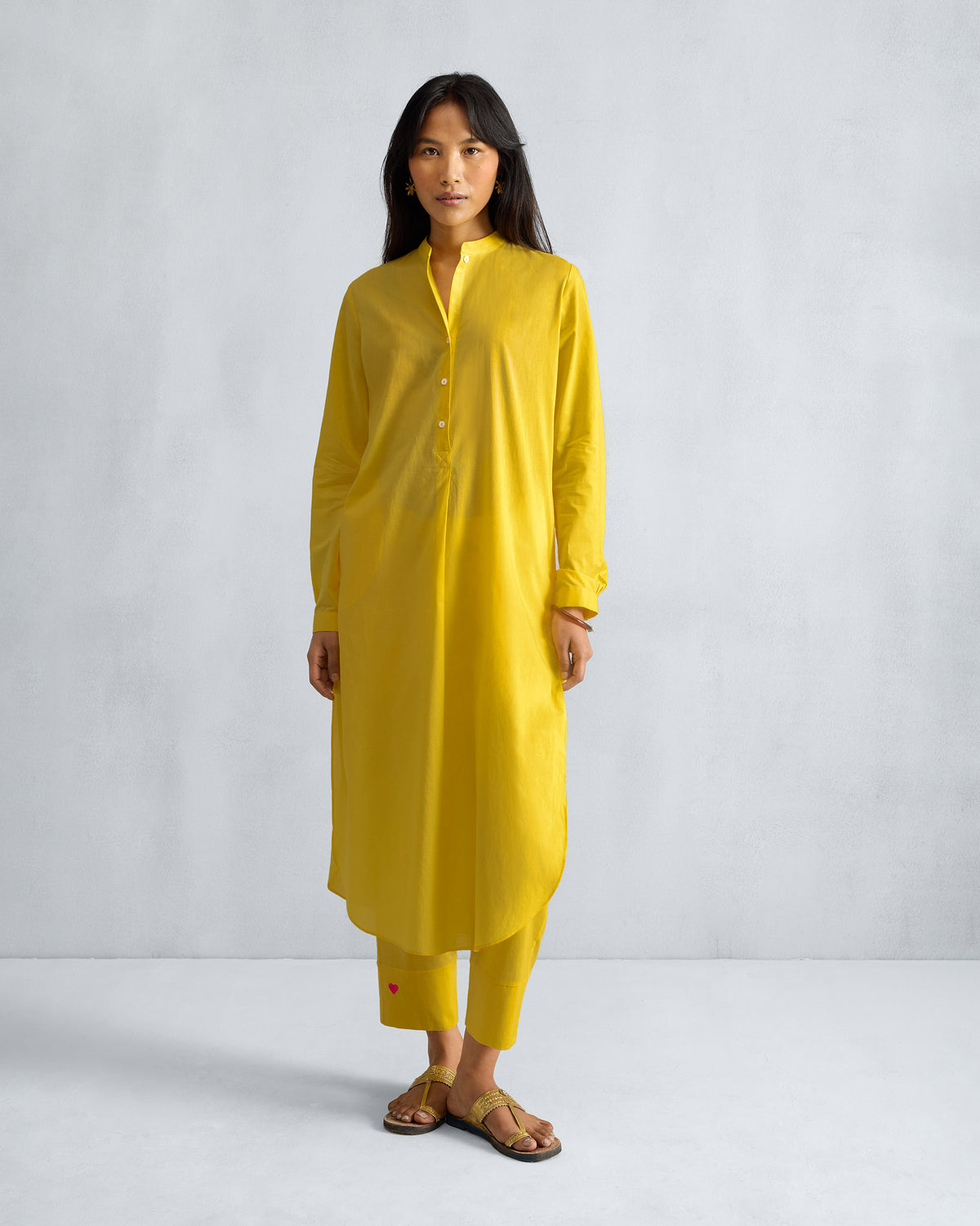 Person wearing a yellow long kurta set with buttoned sleeve cuffs.