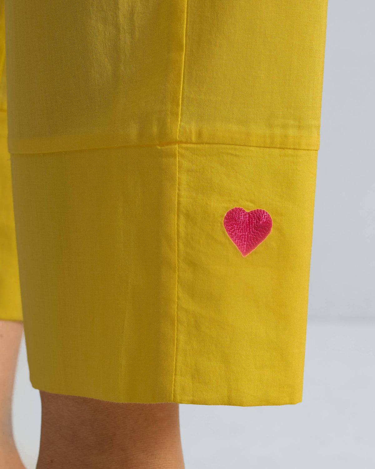Close-up of a pink heart embroidered on the yellow pant hem.