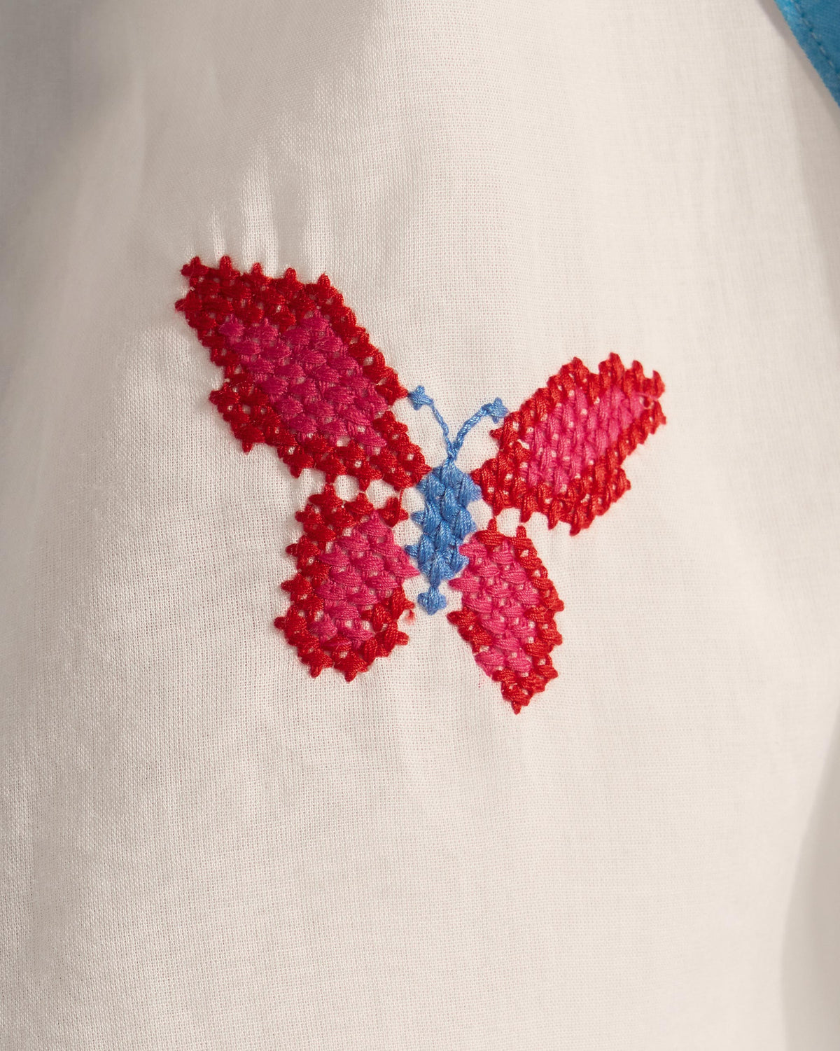 Close-up of a pink and red butterfly embroidery on a white Riha kurta.