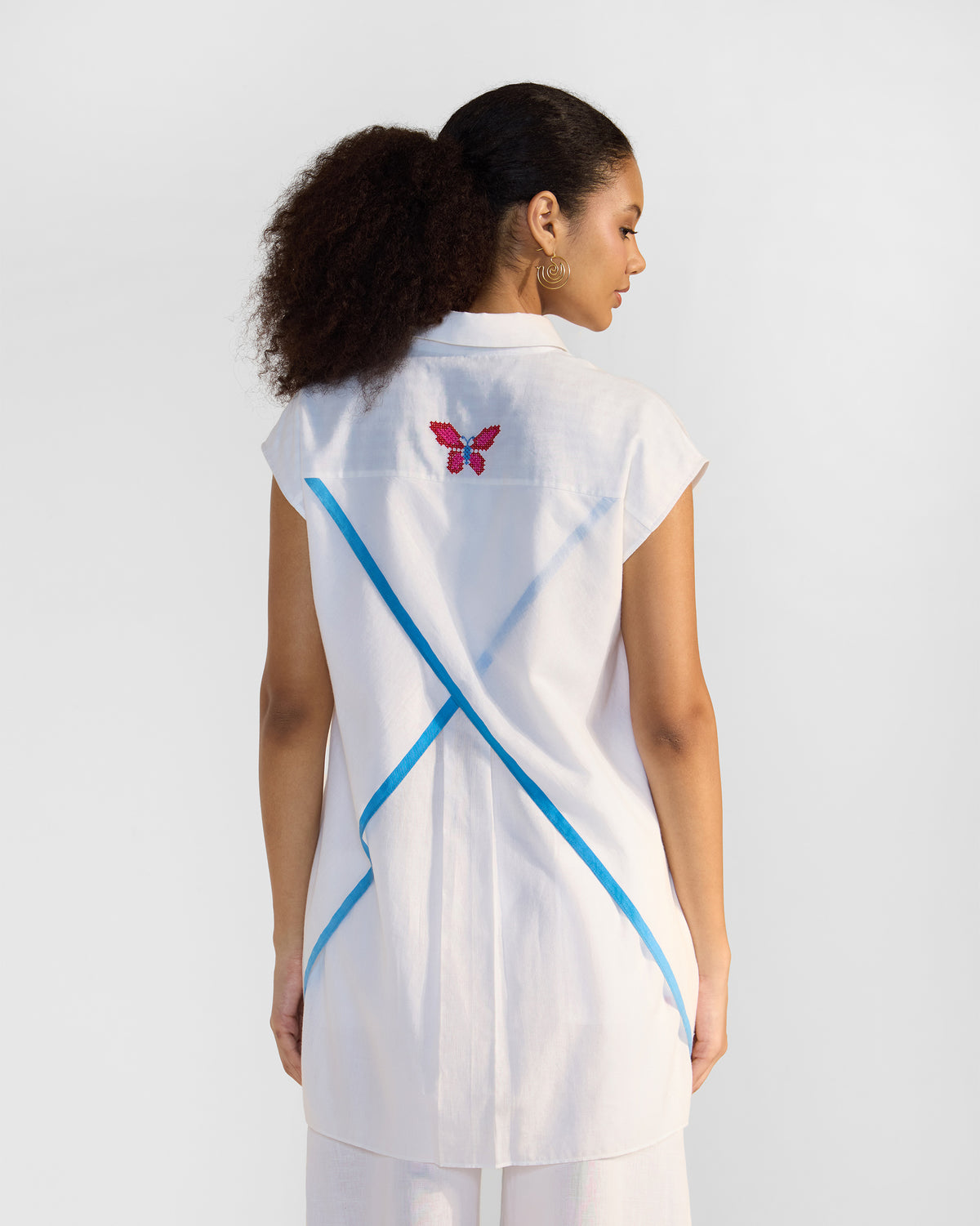 Back of a white Eira top with crossed blue tapes and a butterfly embroidery.