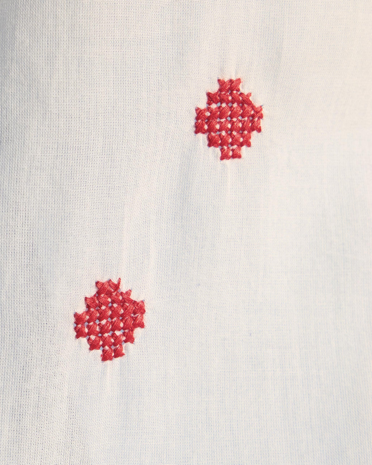 Close-up of red cross-stitch diamond motifs on a white Eira top.