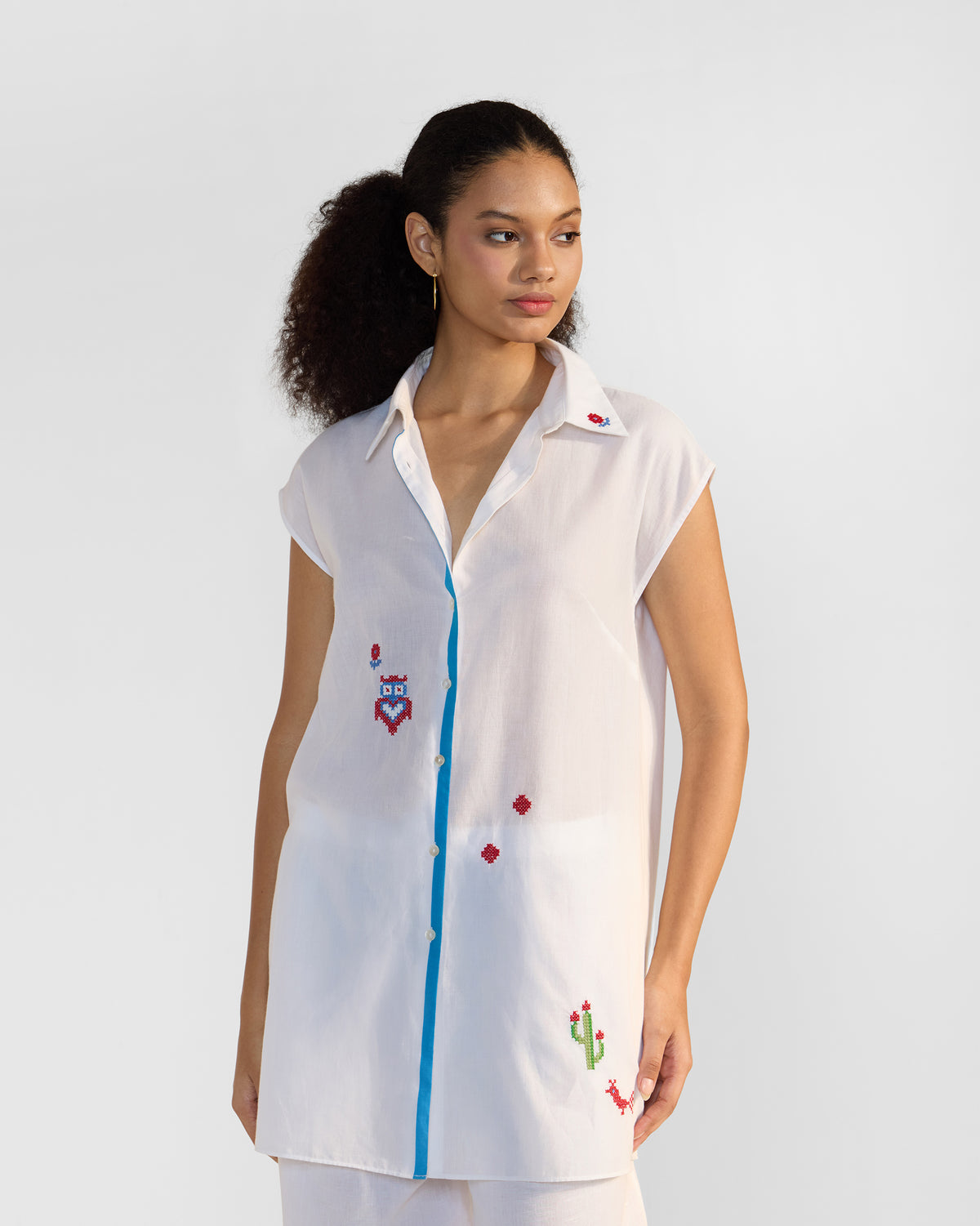 White sleeveless Eira top with blue placket trim and playful cross-stitch motifs.