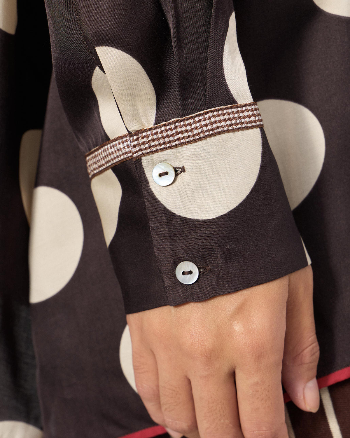 Close-up of a brown polka-dot cuff with check trim and buttons.
