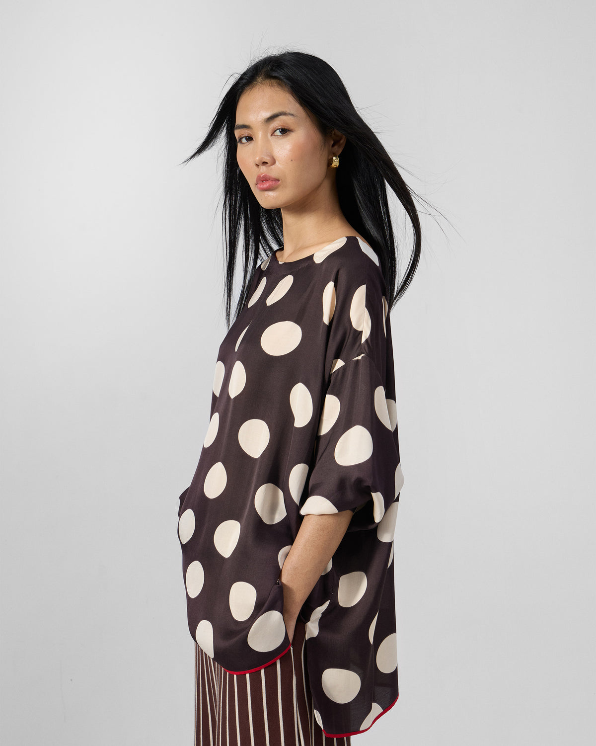 Side view of a brown polka-dot top with a red curved hem.
