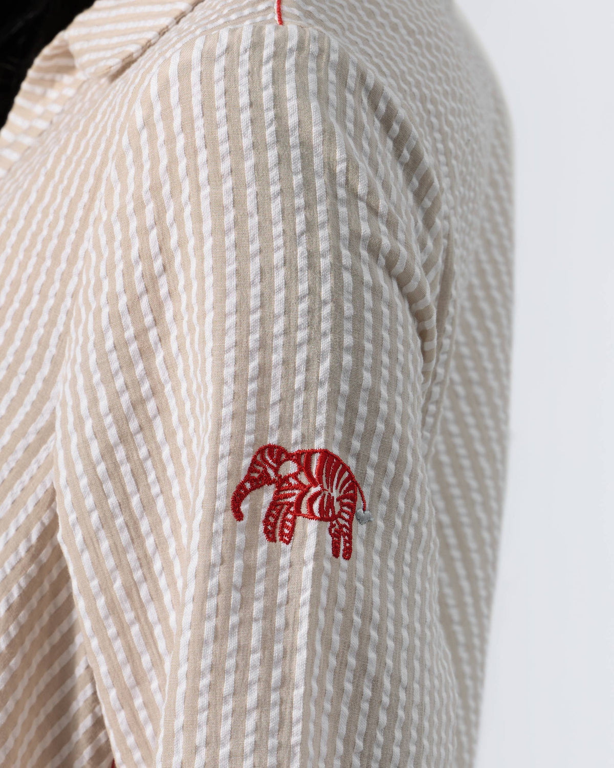 Close-up of a red embroidered elephant on a brown and ivory seersucker sleeve.