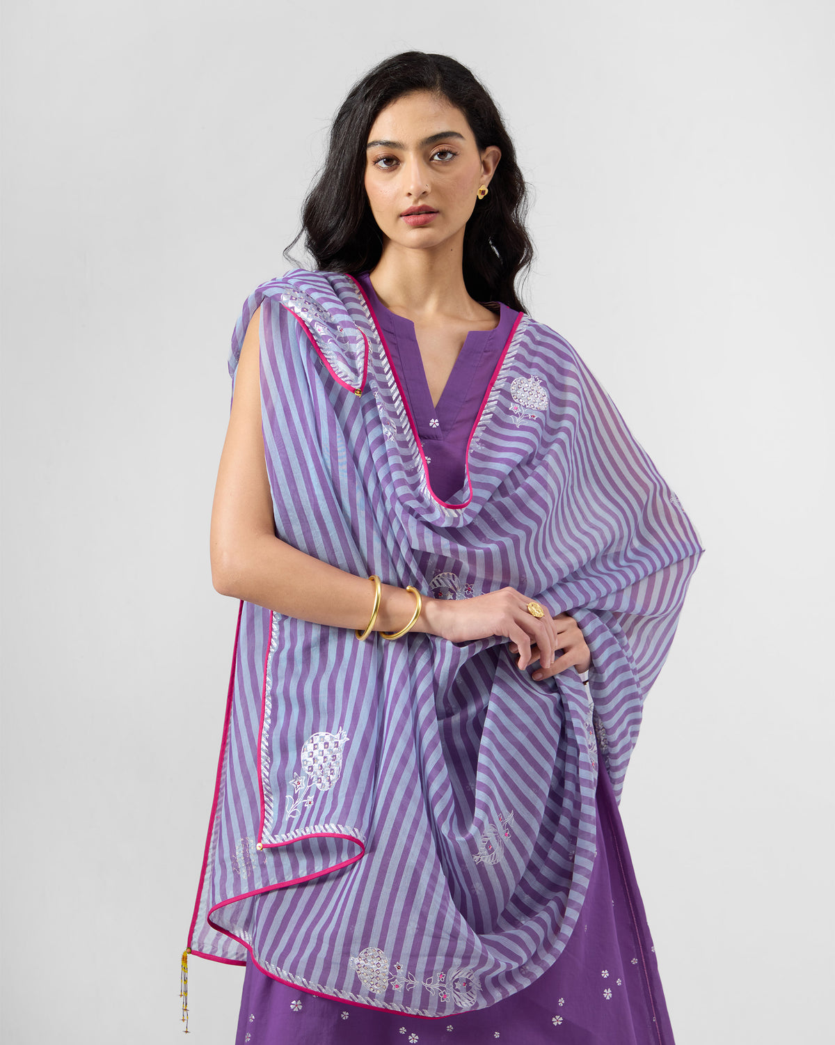 Person wearing a purple kurta set with a striped pink-bordered dupatta.