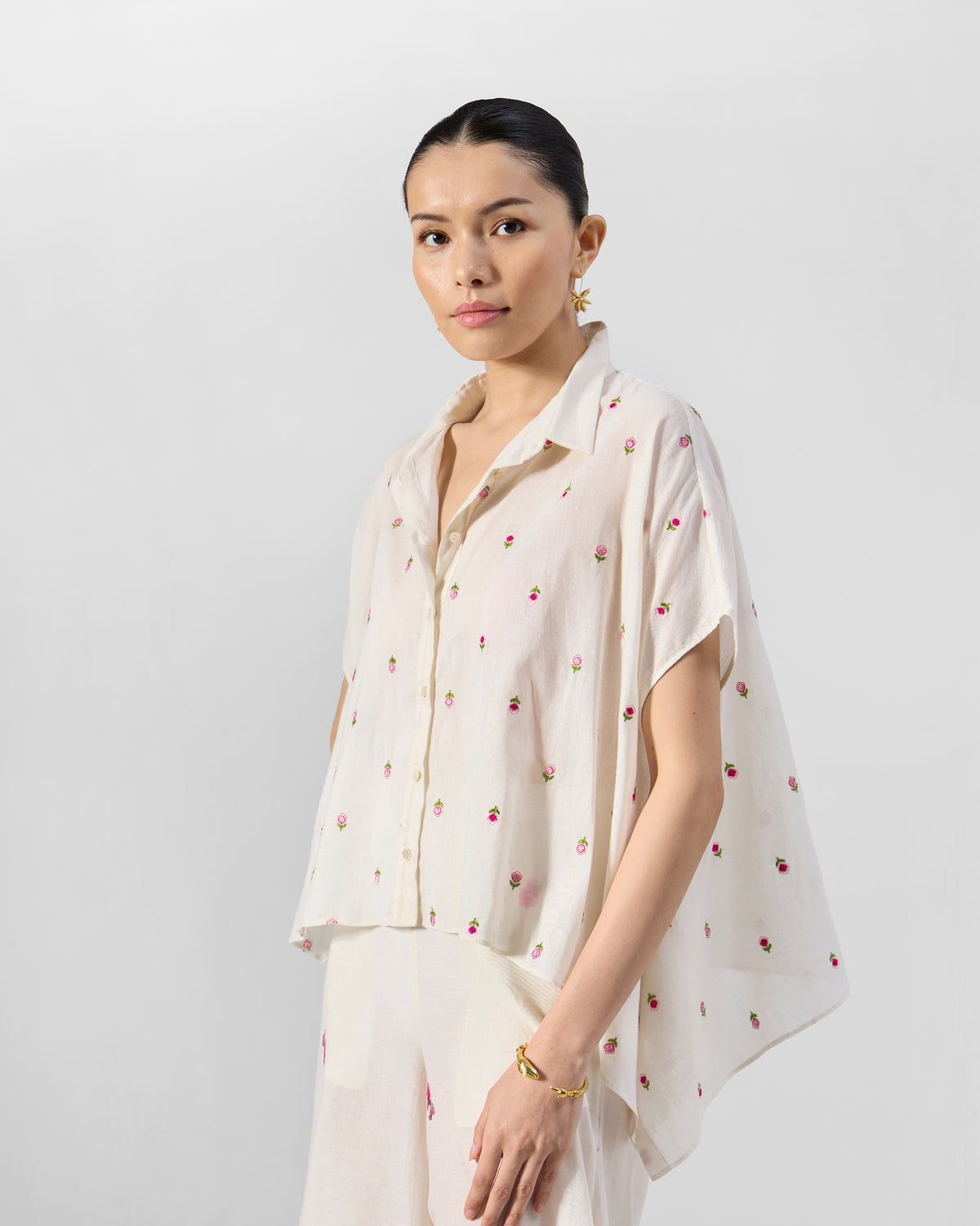 Person wearing an ivory short-sleeve shirt with pink rose embroidery.