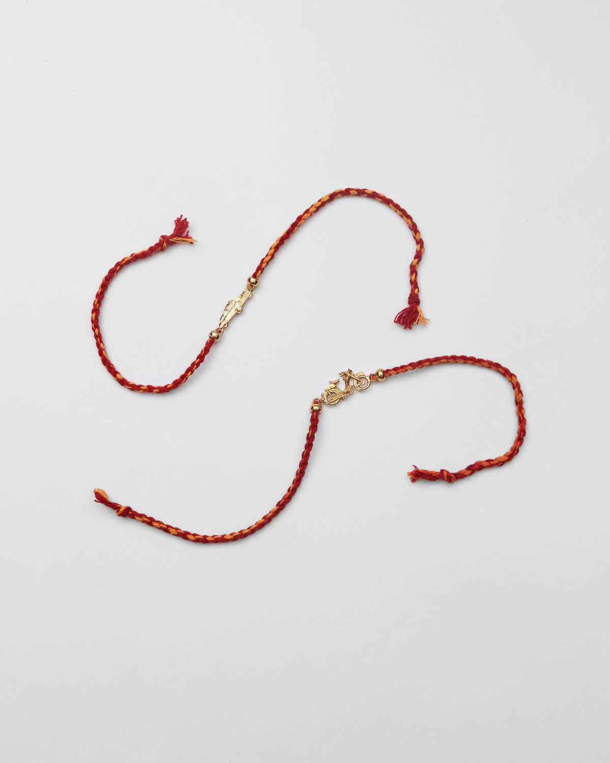 Pair of gold charm rakhis on red and orange braided cords.