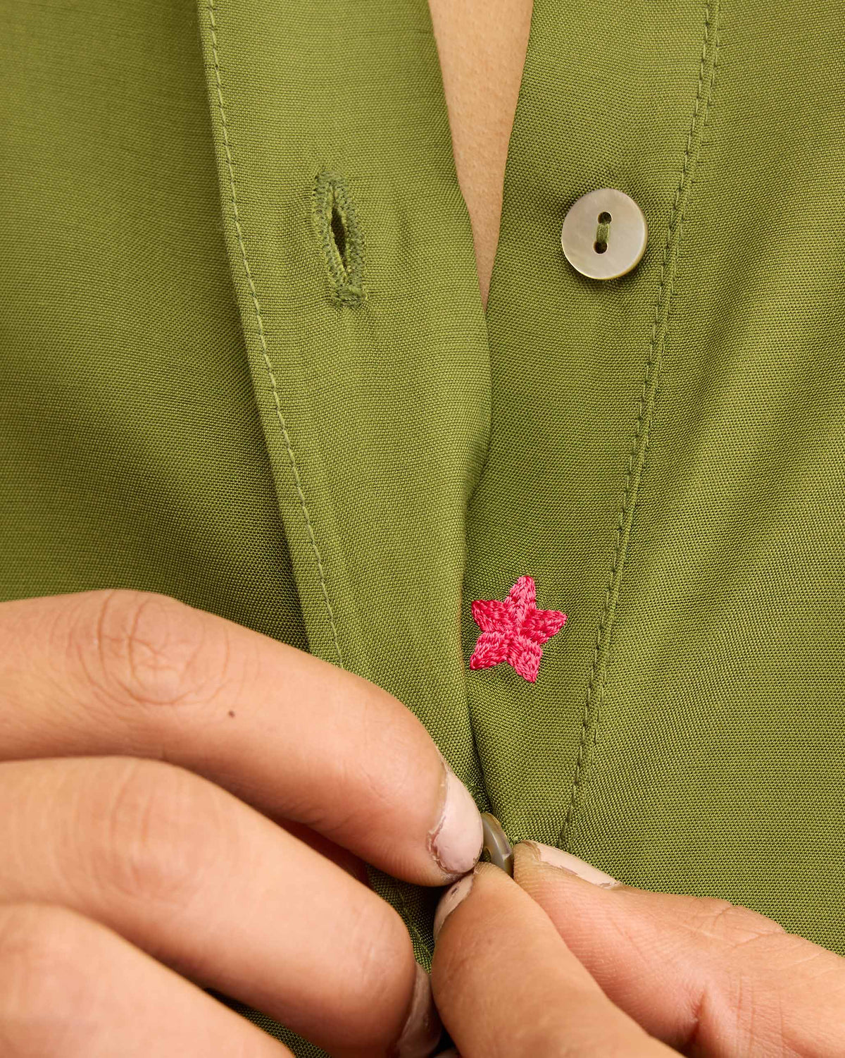 Close-up of an olive kurta placket with a pink embroidered star.