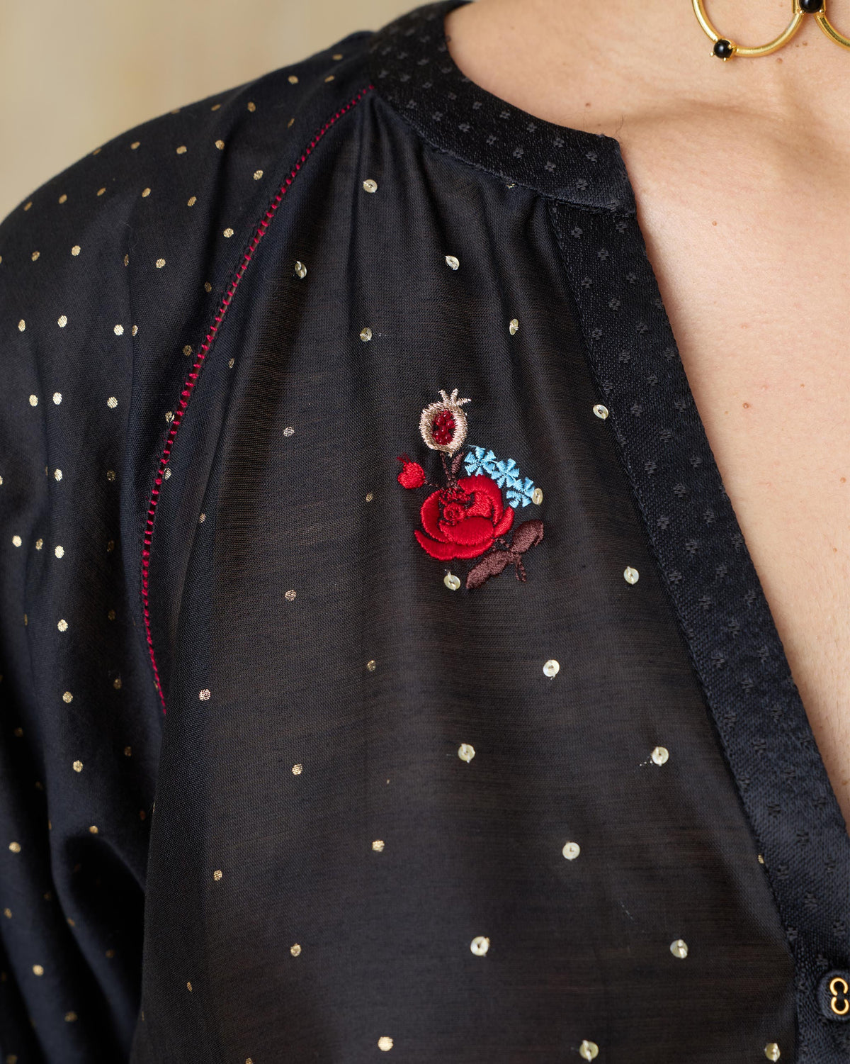 Close-up of a black Moonbeam kurta V-neck with floral embroidery and gold dots.
