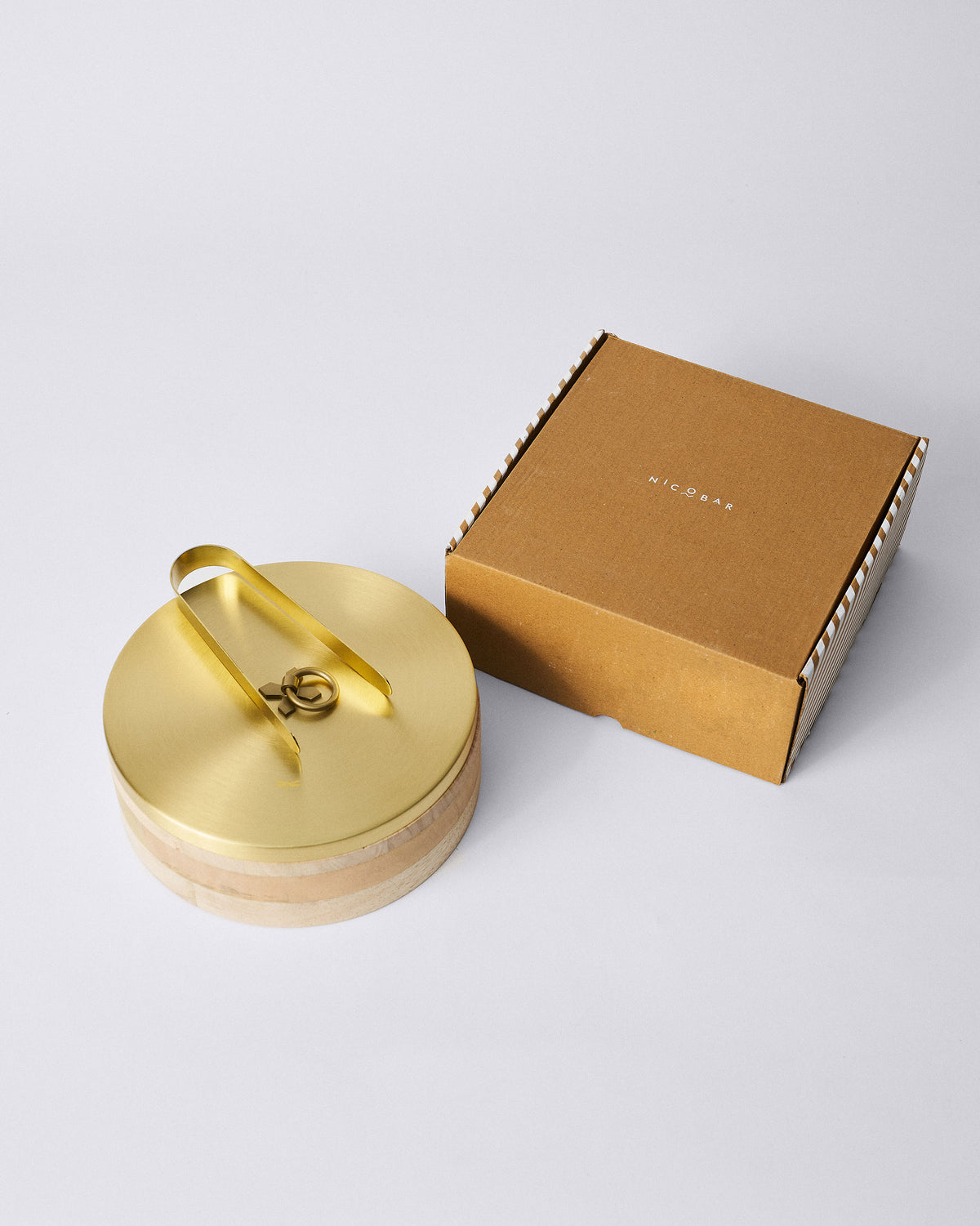 Roti box with brass tongs on the lid beside its striped Nicobar gift box.