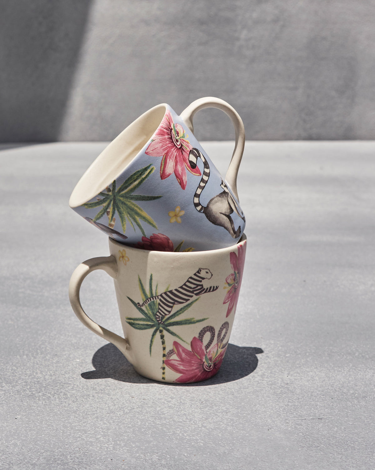 Blue lemur mug stacked on a cream tiger mug with pink tropical flowers.