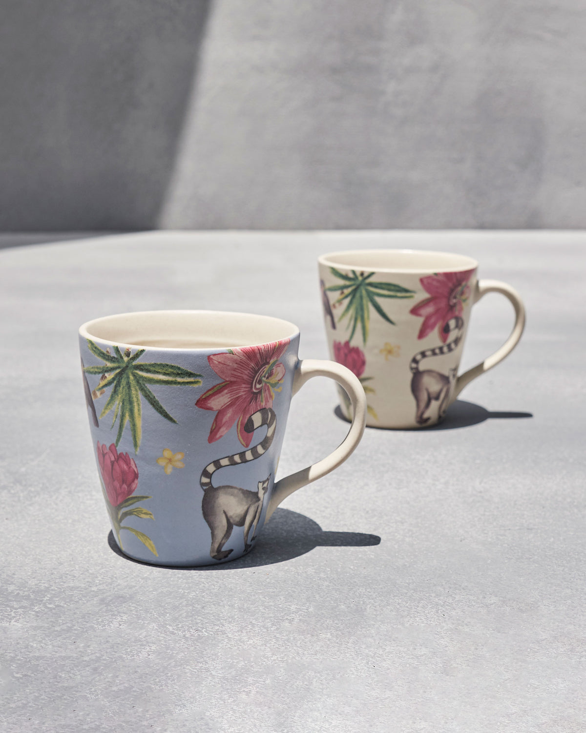 Blue and cream mugs each painted with a ring-tailed lemur and pink flowers.