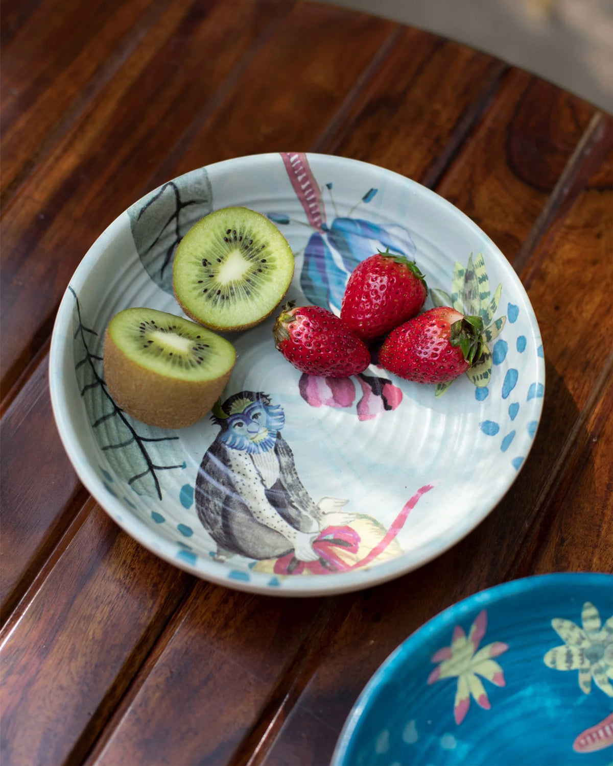 Mahi shallow bowl with monkey motif holding kiwi and strawberries.