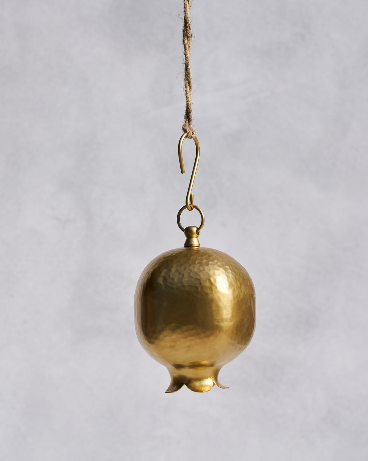 Close-up of a hammered gold Anar pomegranate bell hanging from jute twine.