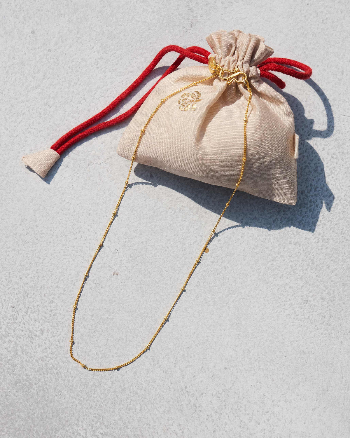 Extra small Boondi Chain in gold laid beside a cream drawstring pouch.