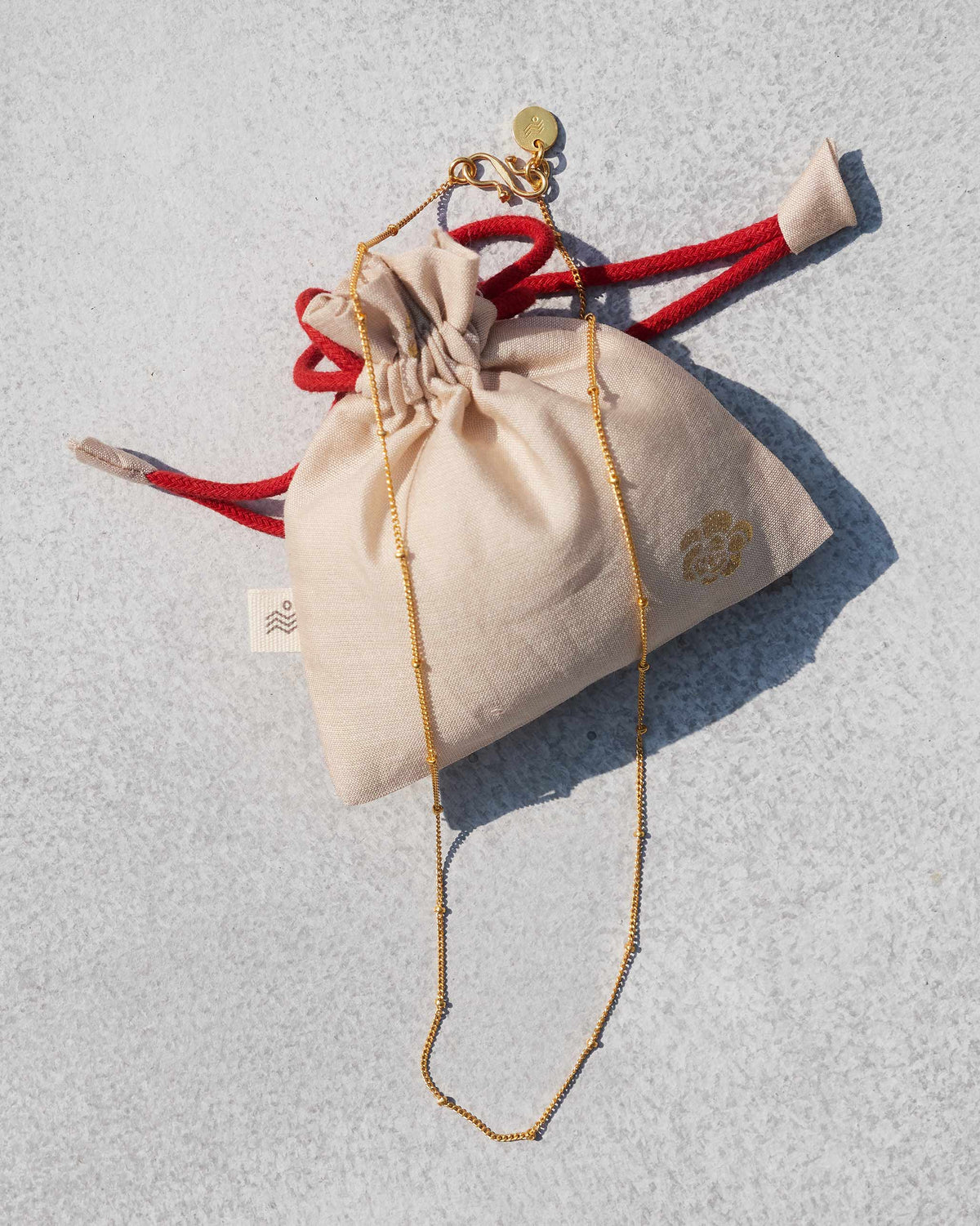 Small Boondi Chain in gold laid beside a cream drawstring pouch.