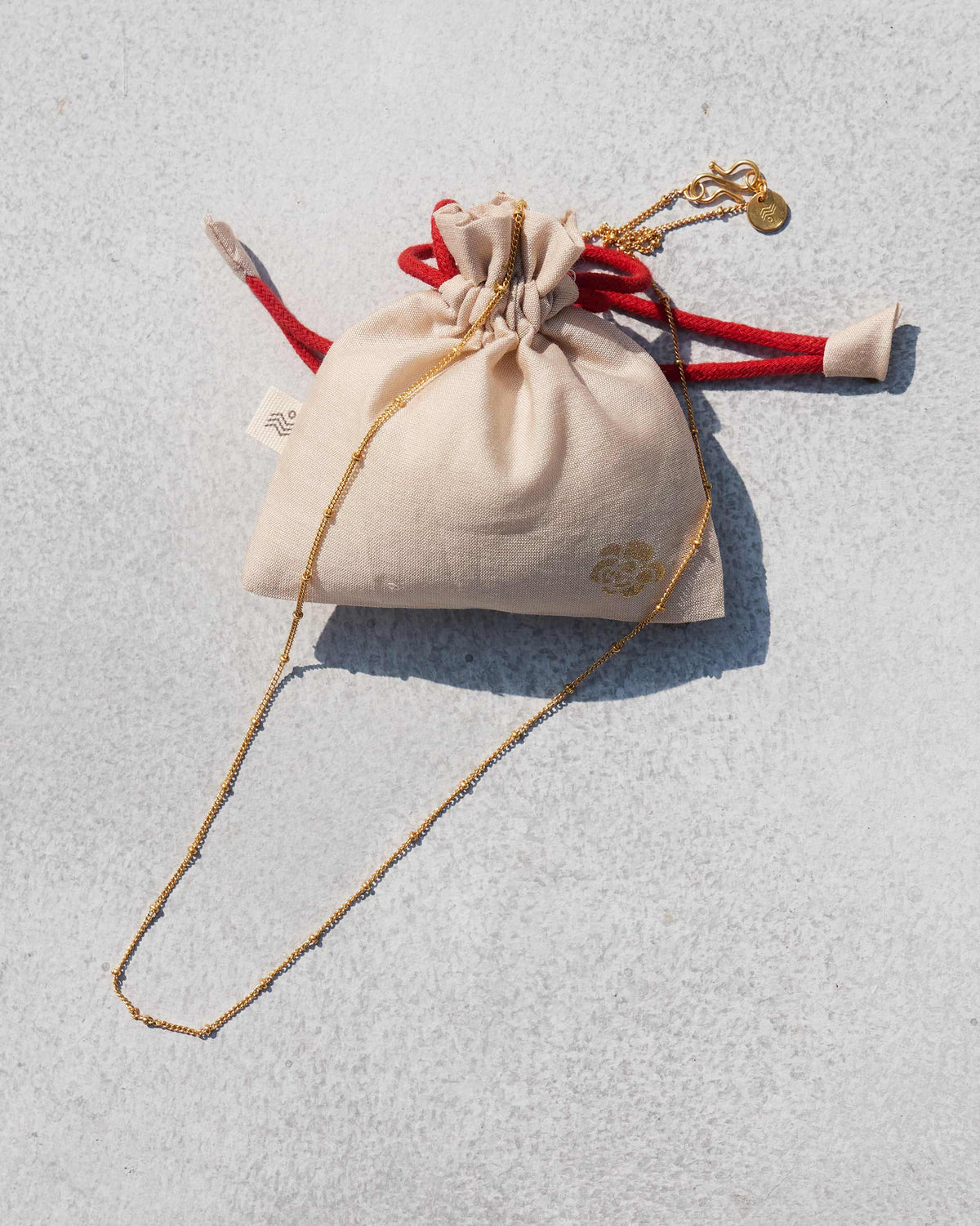 Medium Boondi Chain in gold laid beside a cream drawstring pouch.
