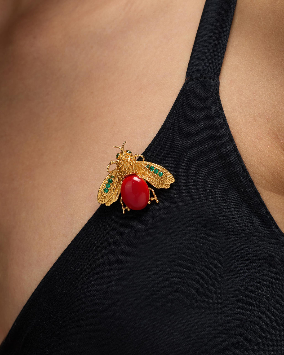 Gold Bug brooch with a red stone body pinned on a black strap.