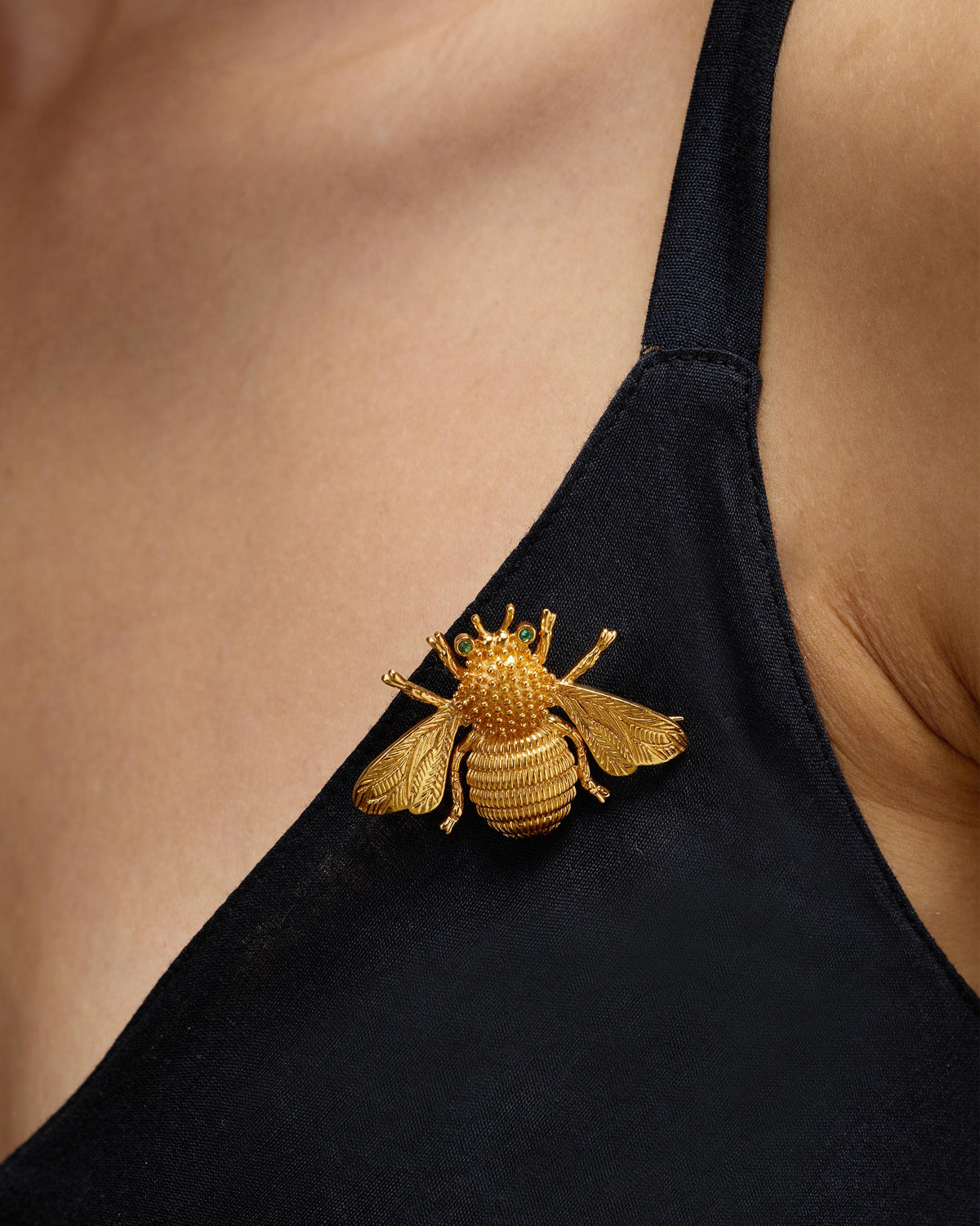 Close-up of a gold Bee brooch with green eyes pinned to a black top.
