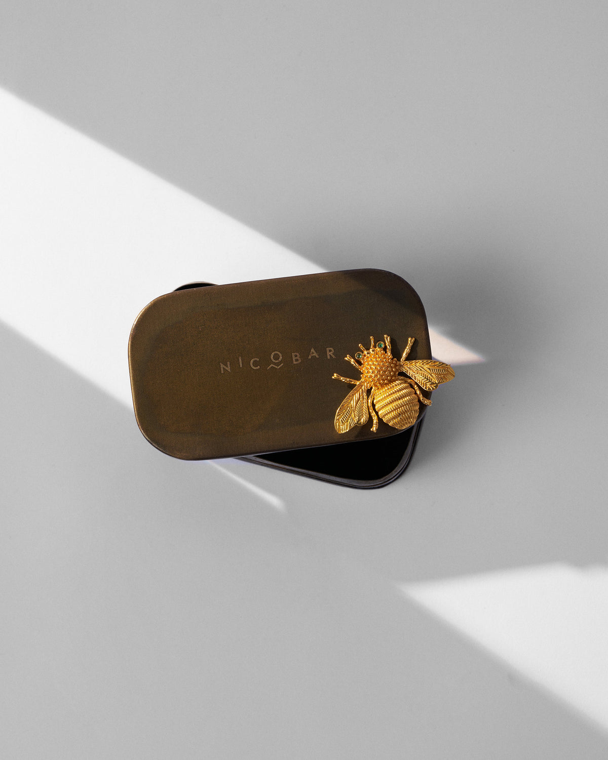 Gold Bee brooch resting on a dark Nicobar metal tin.