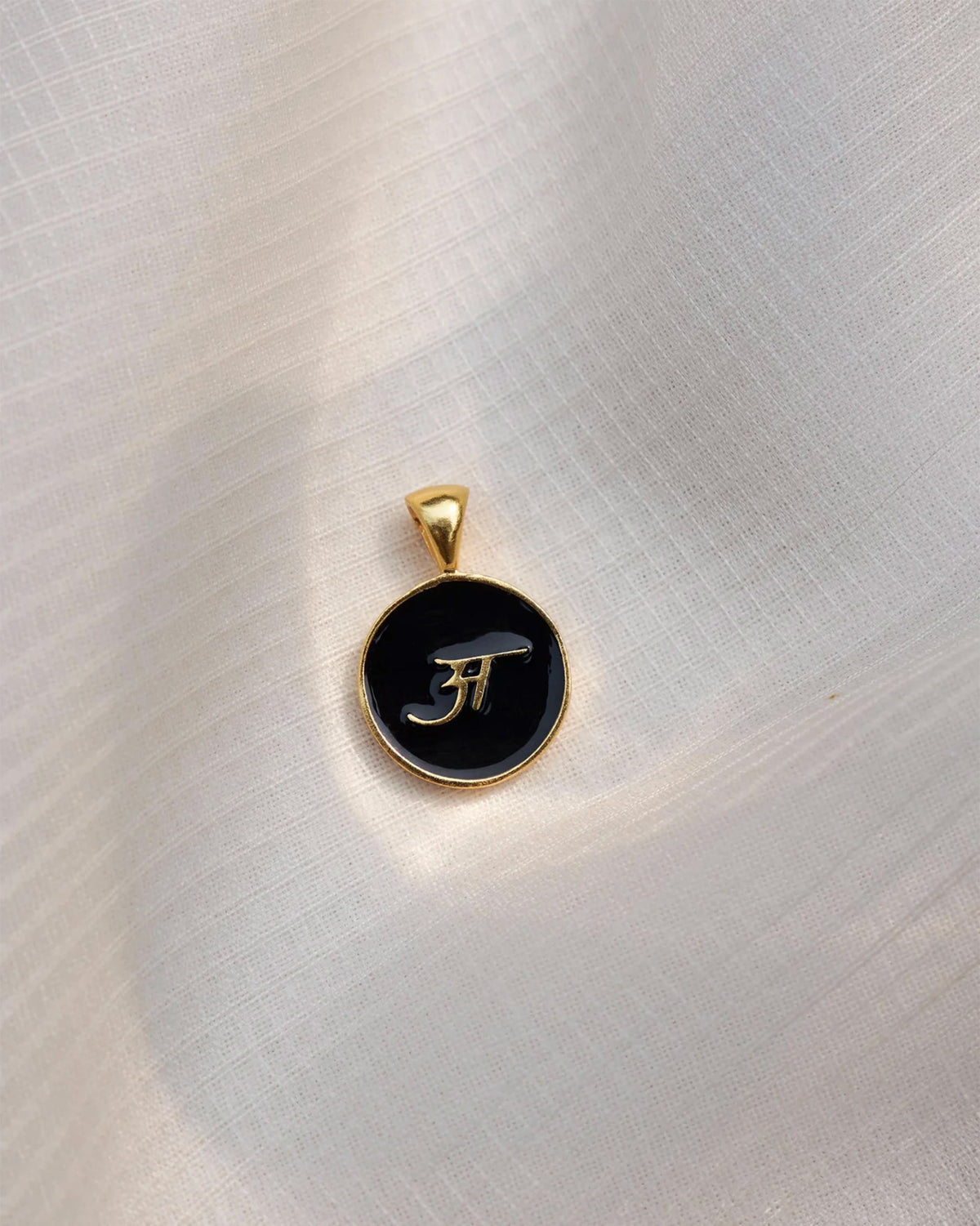 Close-up of a black and gold Alphabet A charm showing अ.
