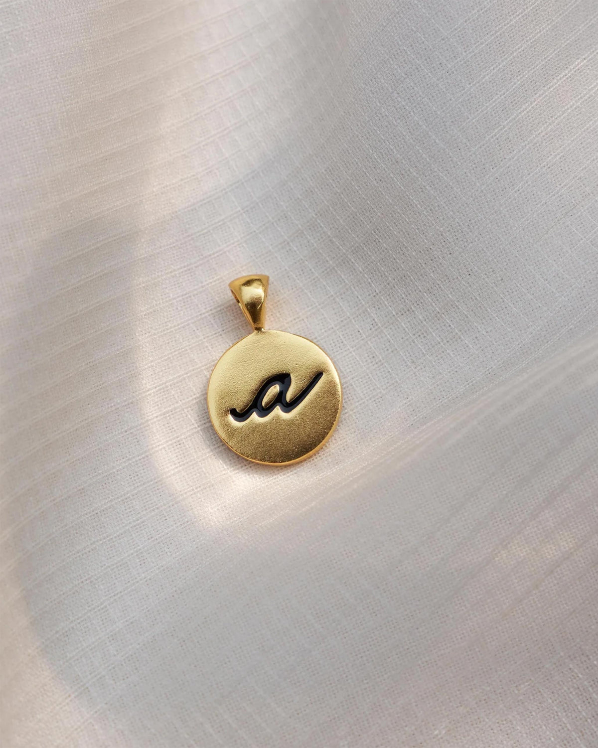 Close-up of a gold Alphabet A charm with a black script a.