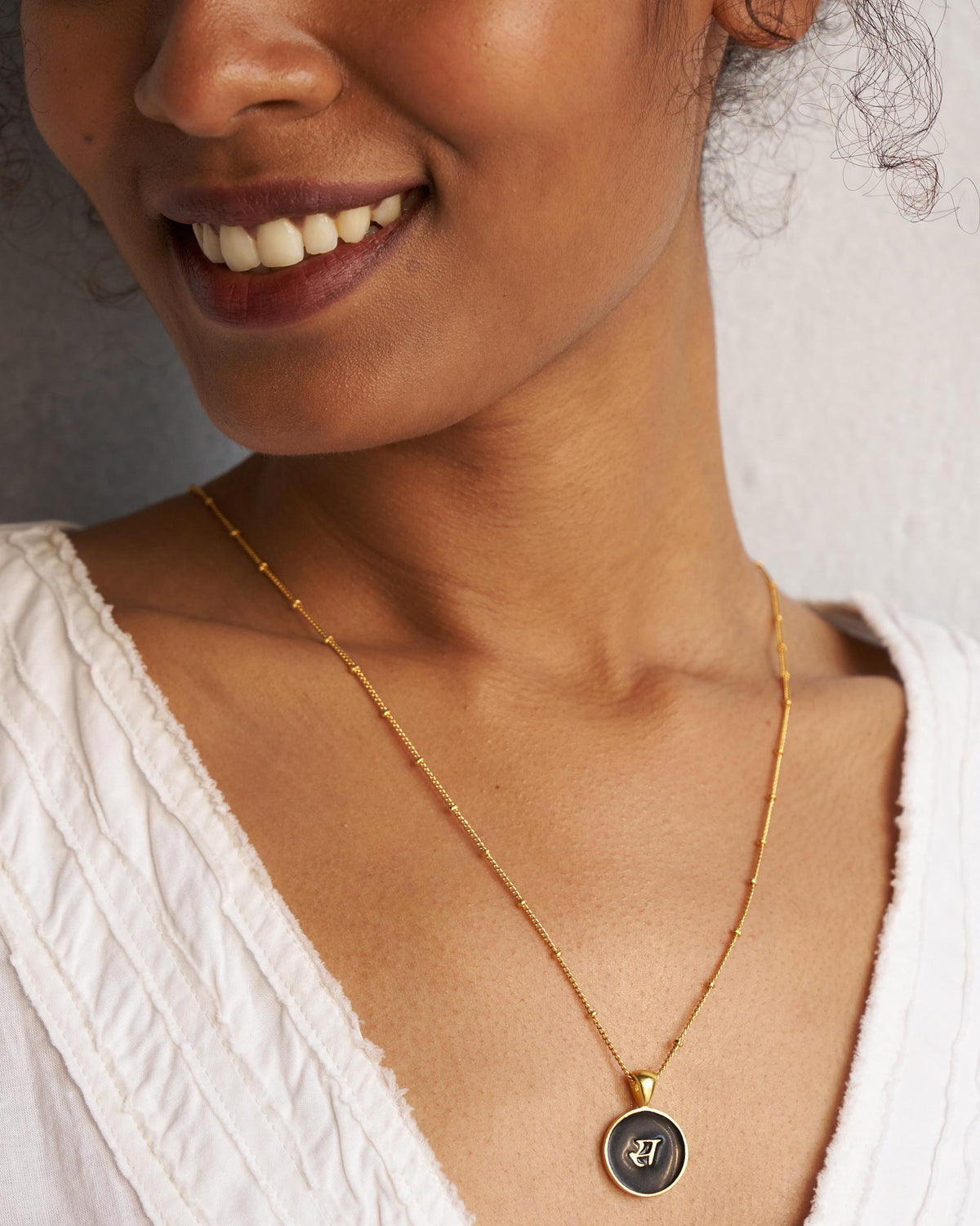 Gold satellite chain with a black enamel charm showing a Devanagari letter.