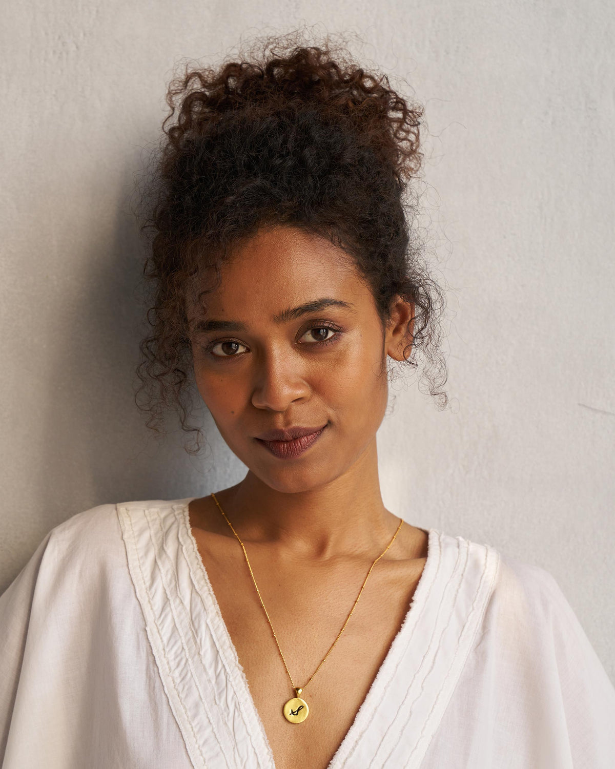Person wearing a gold satellite chain with a circular alphabet charm.