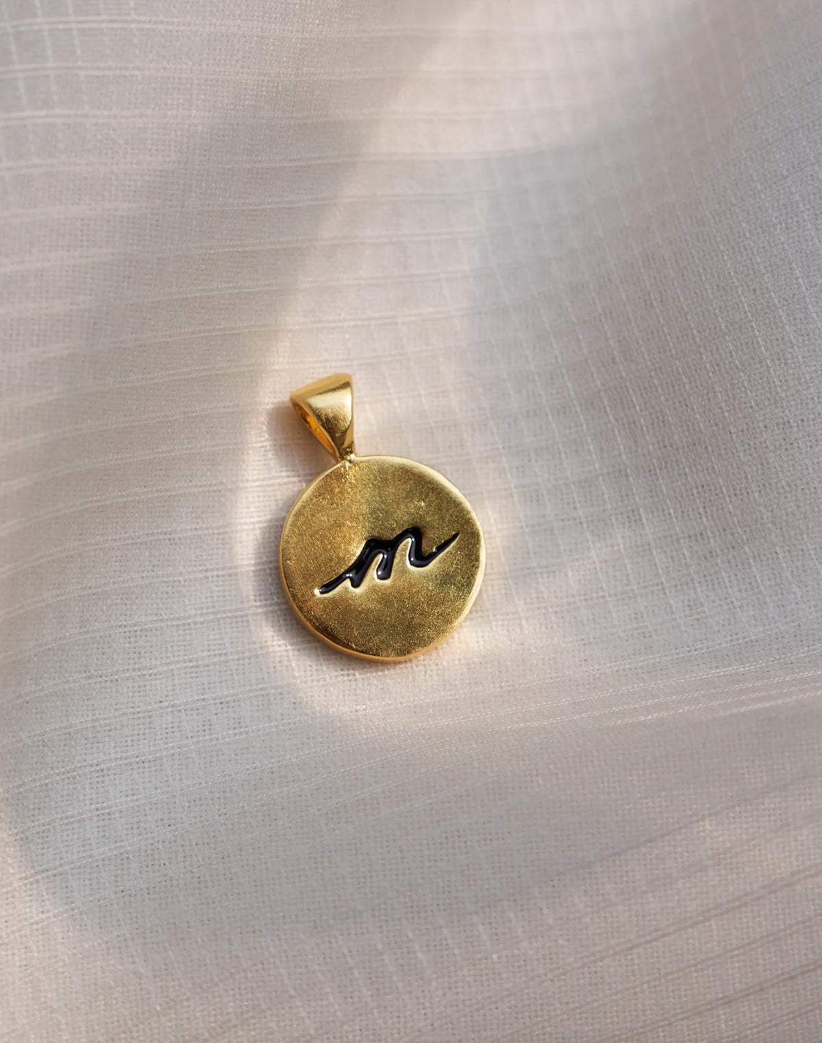 Alphabet M charm with a black script m on a gold face.