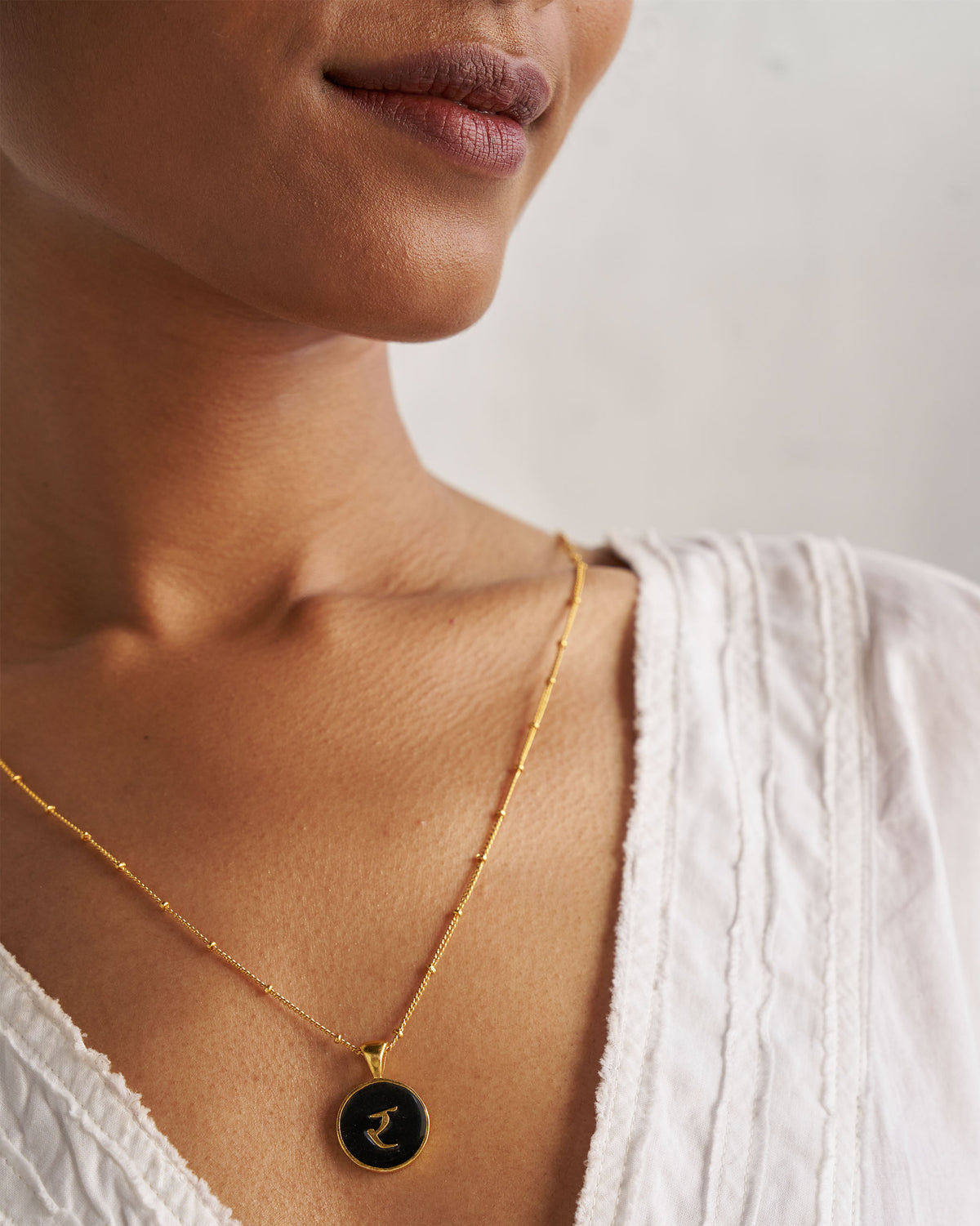 Black and gold Alphabet R charm with र worn on a satellite chain.