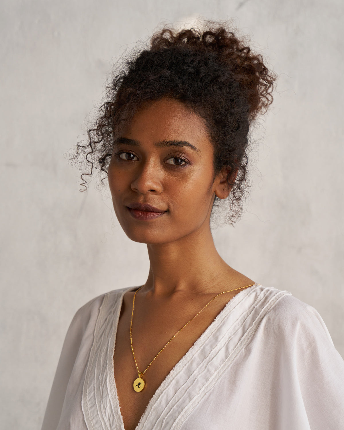 Person wearing a gold Alphabet R charm on a fine chain.