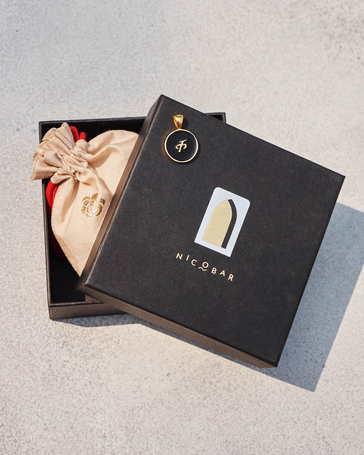 Black and gold Alphabet K charm with क on a Nicobar gift box.