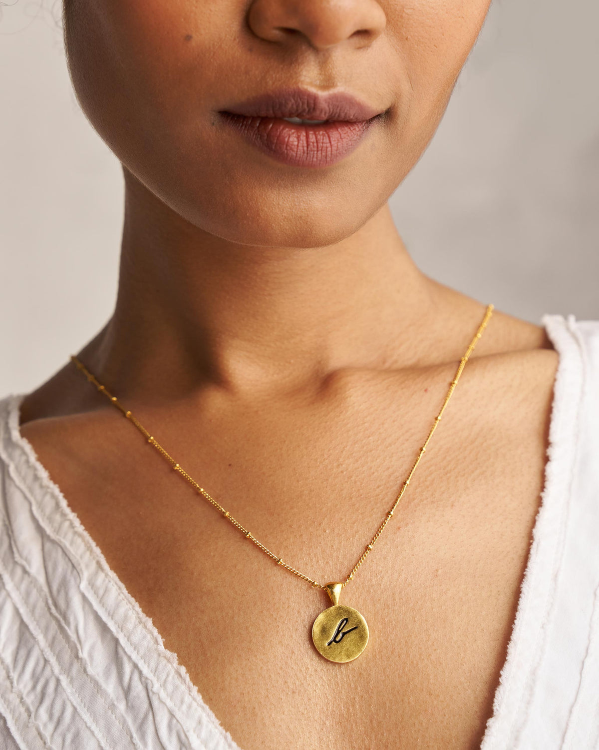 Alphabet B charm with a black script b worn on a gold chain.
