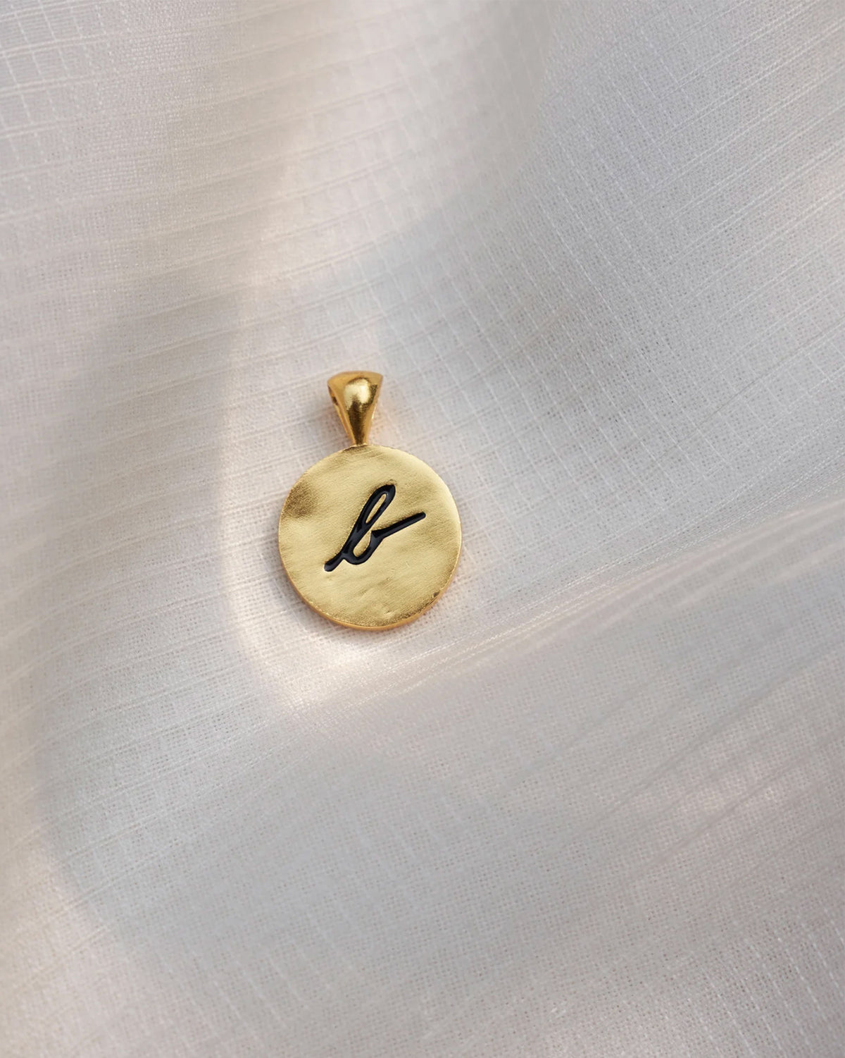 Close-up of a gold Alphabet B charm with a black script b.