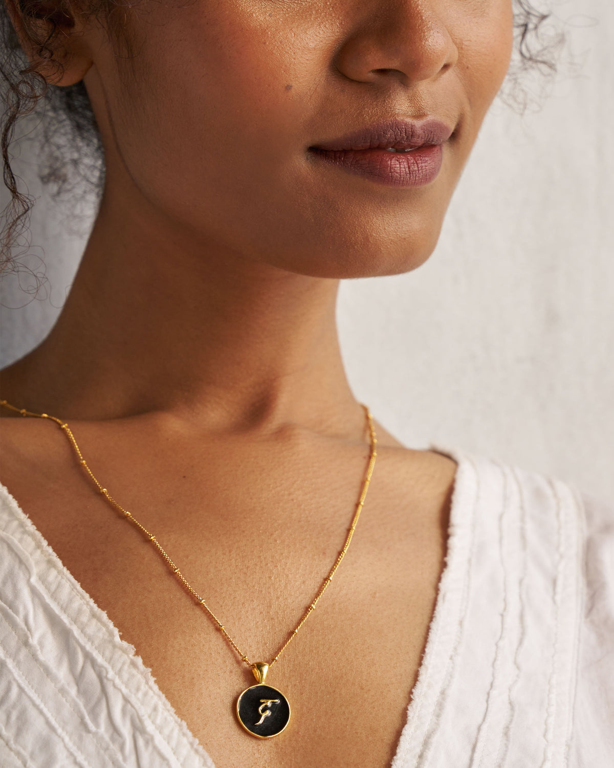 Alphabet D charm in black and gold worn on a fine gold chain.