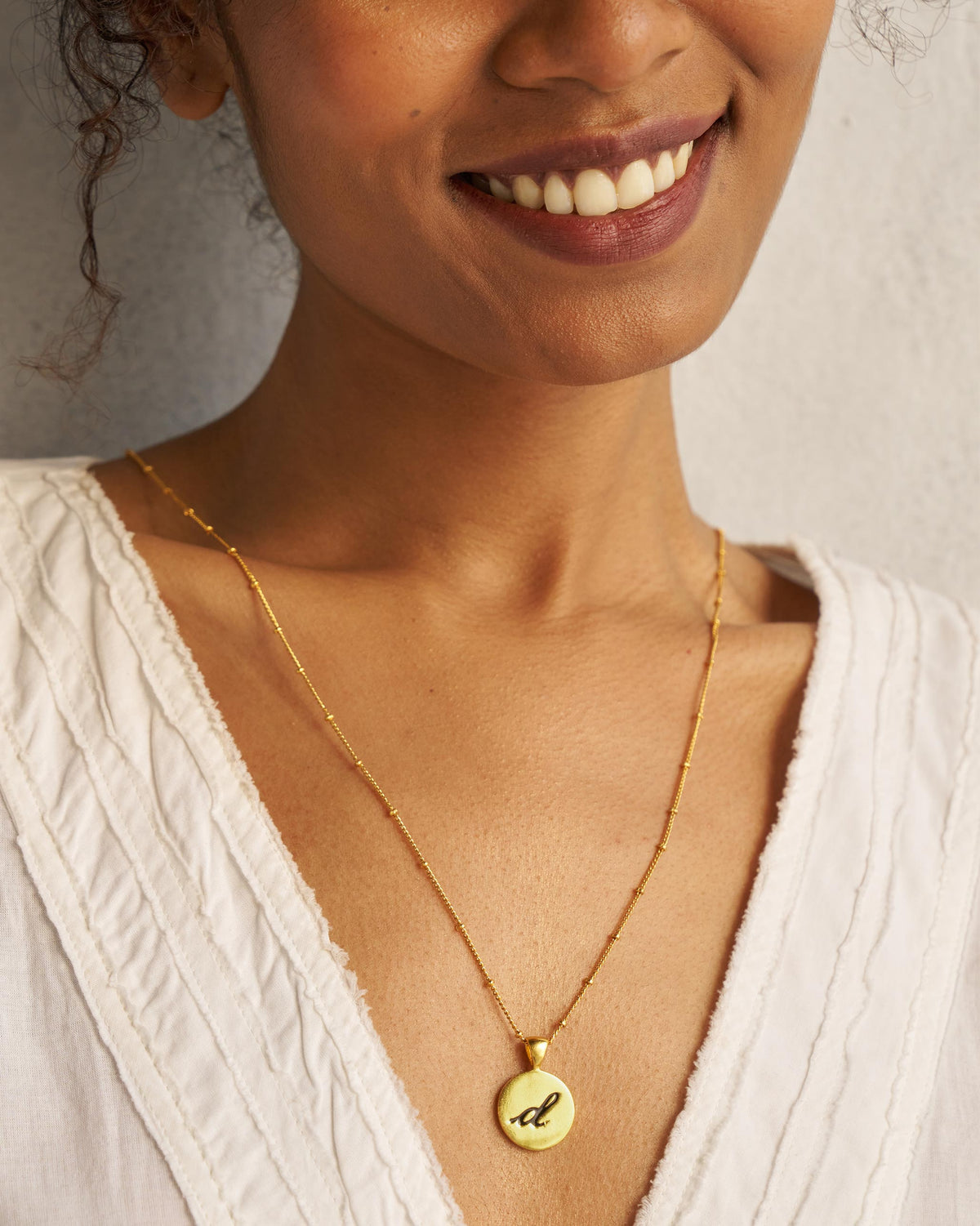 Alphabet D charm with a black script d worn on a gold chain.