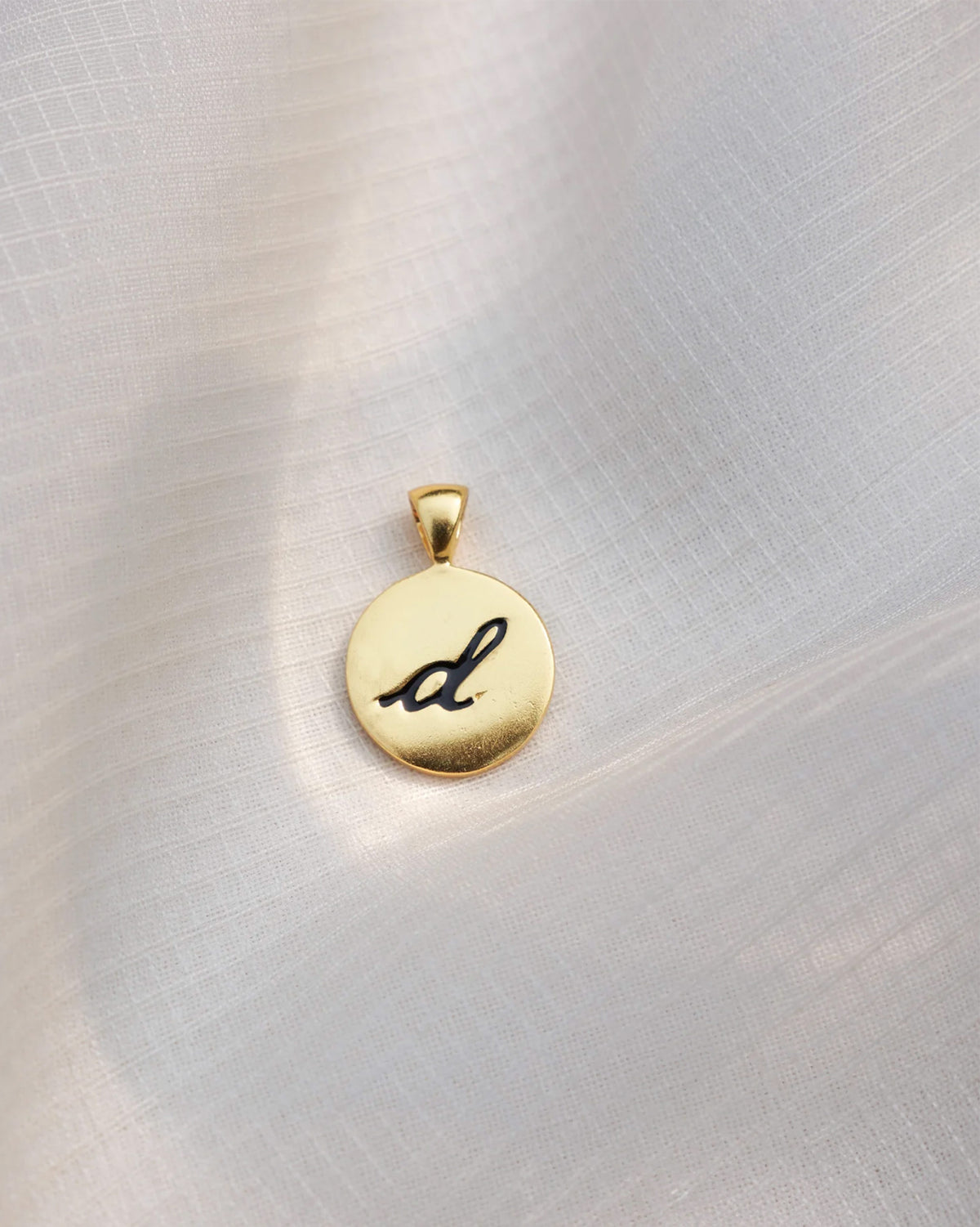 Close-up of a gold Alphabet D charm with a black script d.