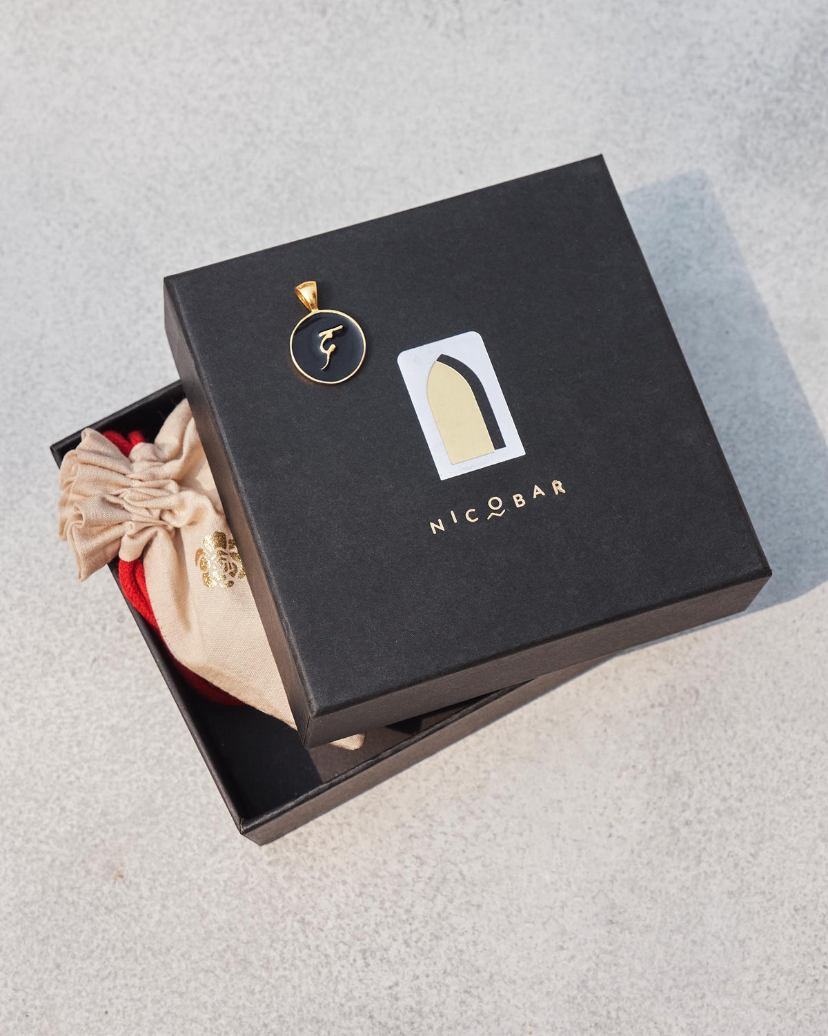 Alphabet D charm in black and gold on a Nicobar gift box.