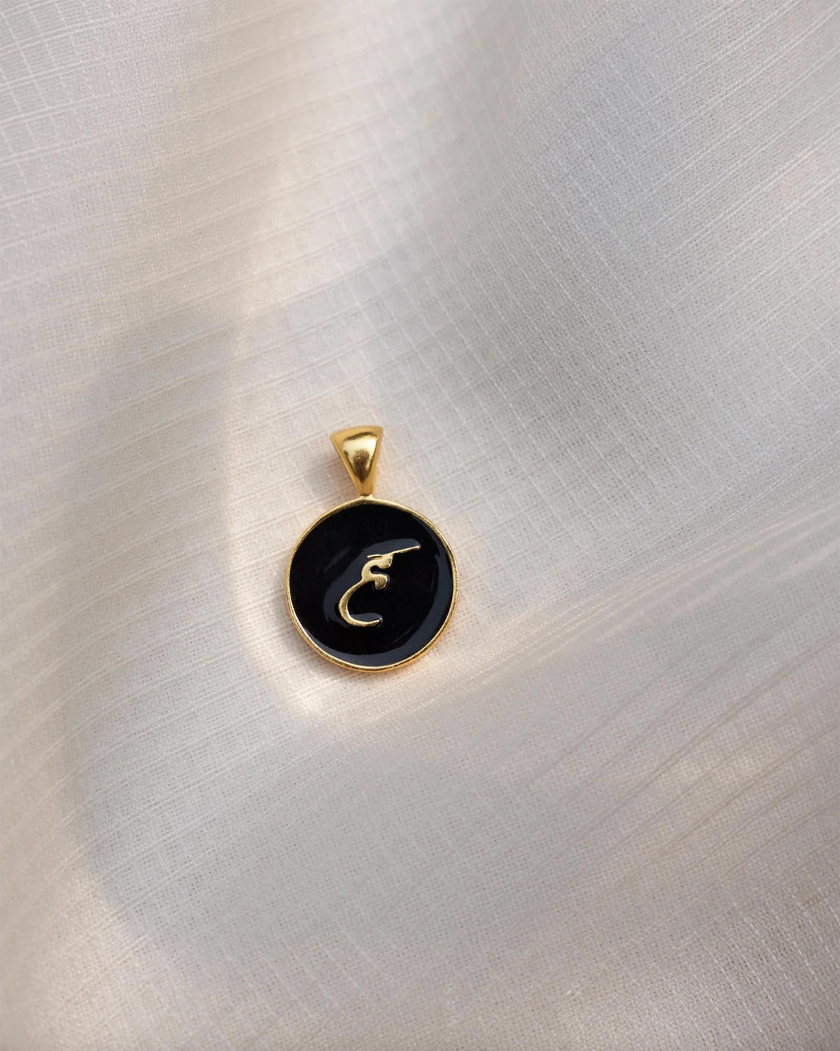 Close-up of a black and gold Alphabet H charm showing a Devanagari letter.