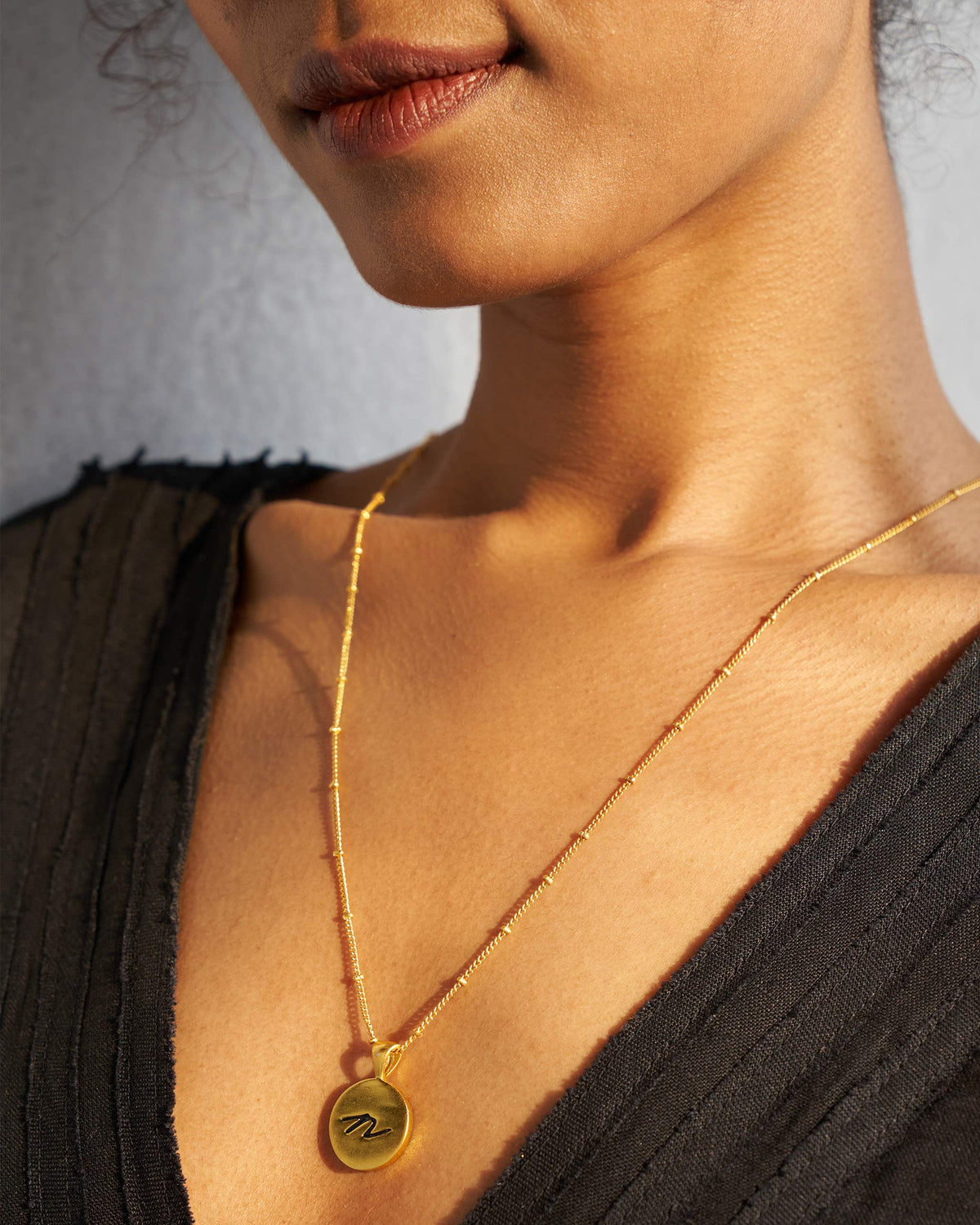 Gold Alphabet N charm with a black script letter n when worn.